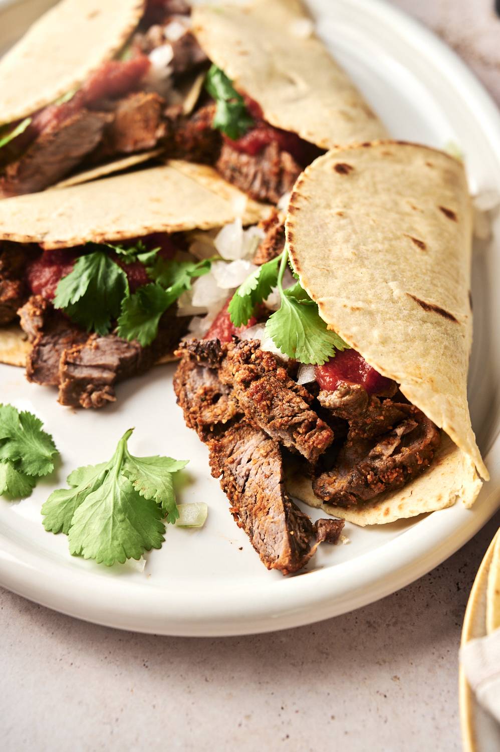 Side view of the steak taco filled with juicy beef, chopped onions, fresh cilantro and salsa sauce, topped with extra cilantro leaves.