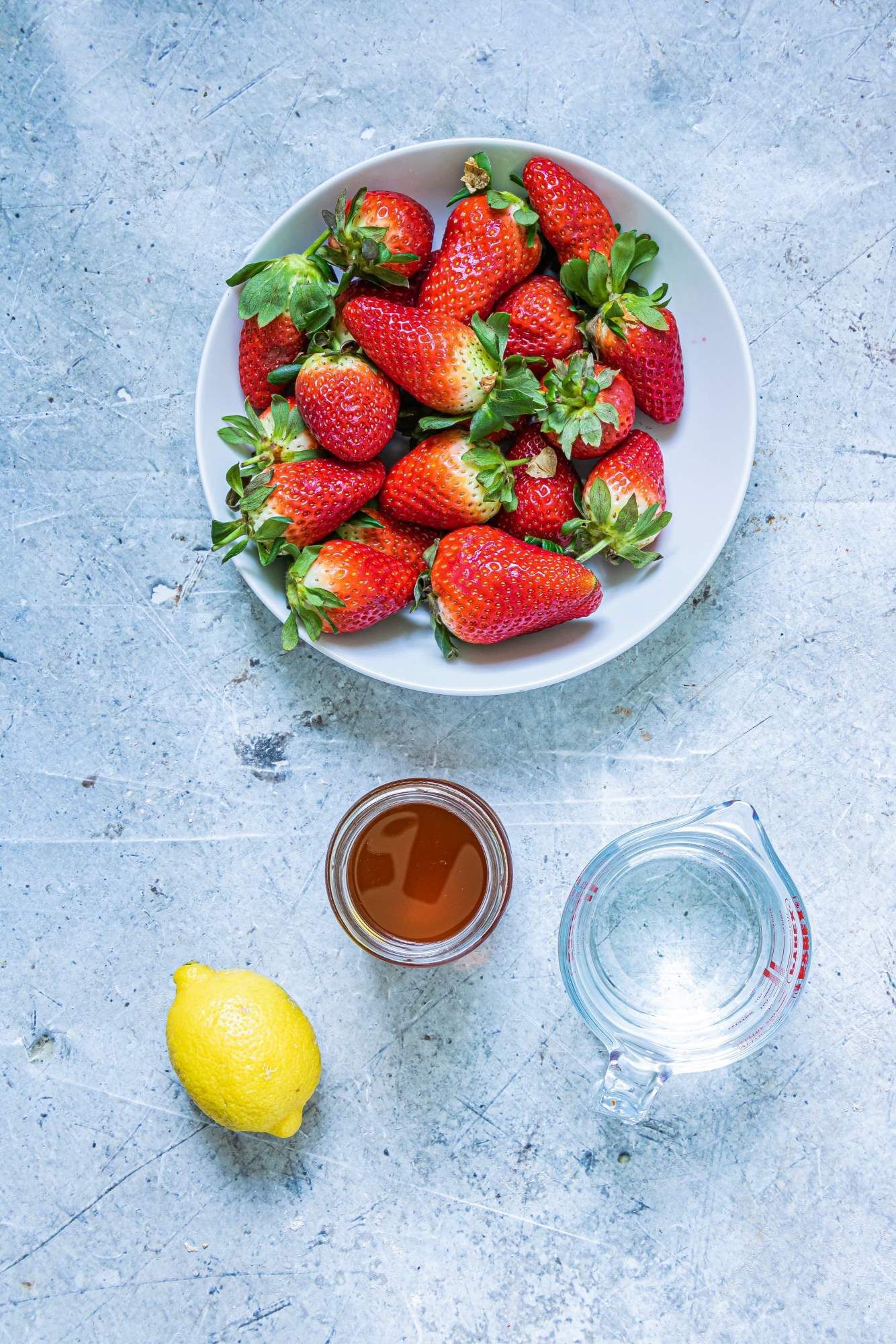 Ingredients for making strawberry popsicles, including fresh strawberries, honey, water and lemon juice.