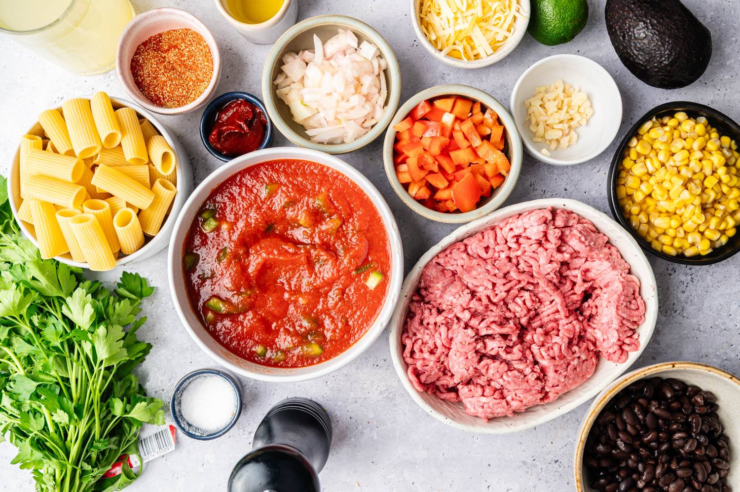 Colorful ingredients including pasta, ground beef, tomato sauce, diced vegetables, corn, black beans and herbs are neatly arranged on the countertop.