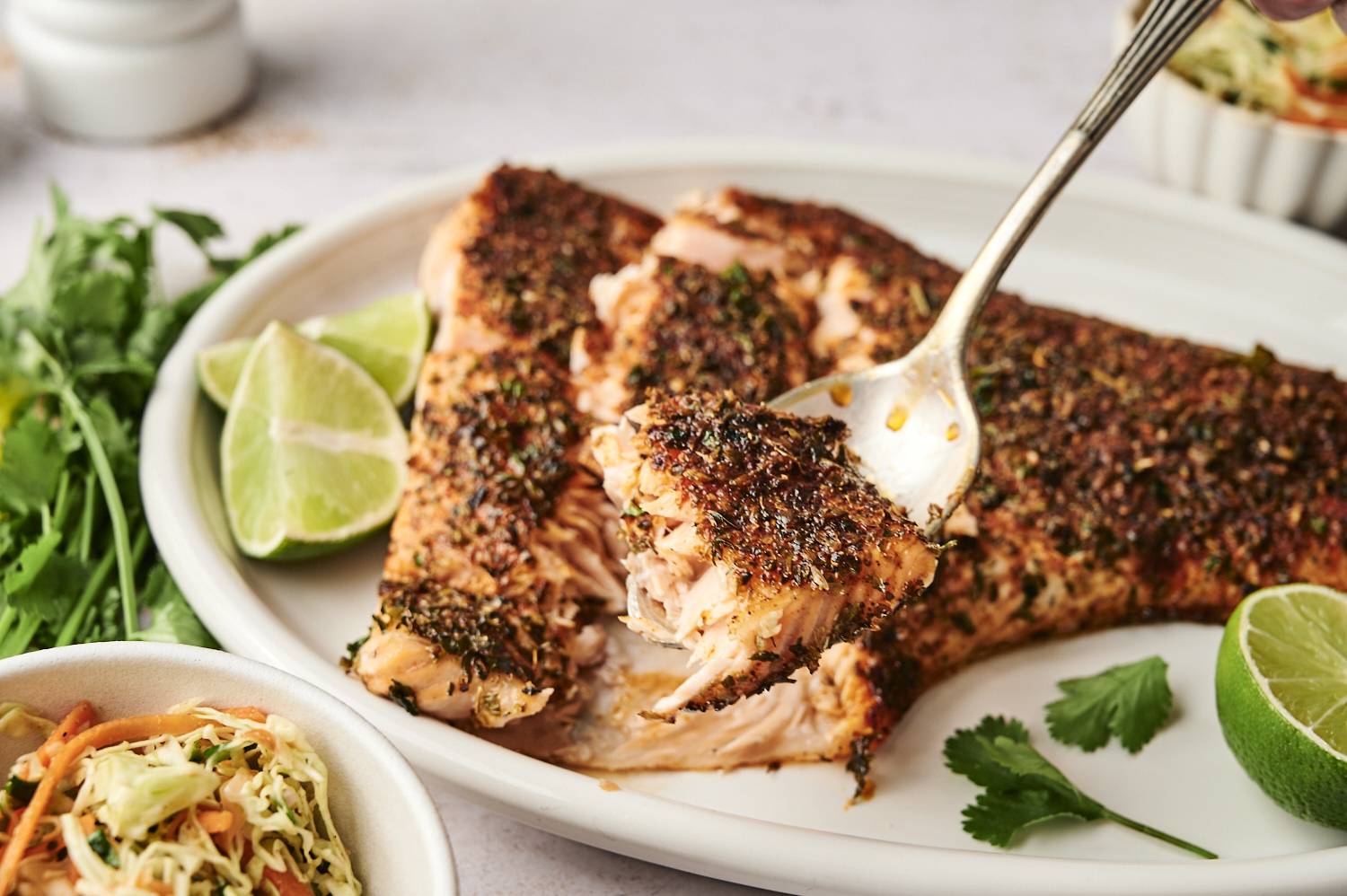 A spiced salmon fillet is served with fresh lime wedges and slaw on a white plate.