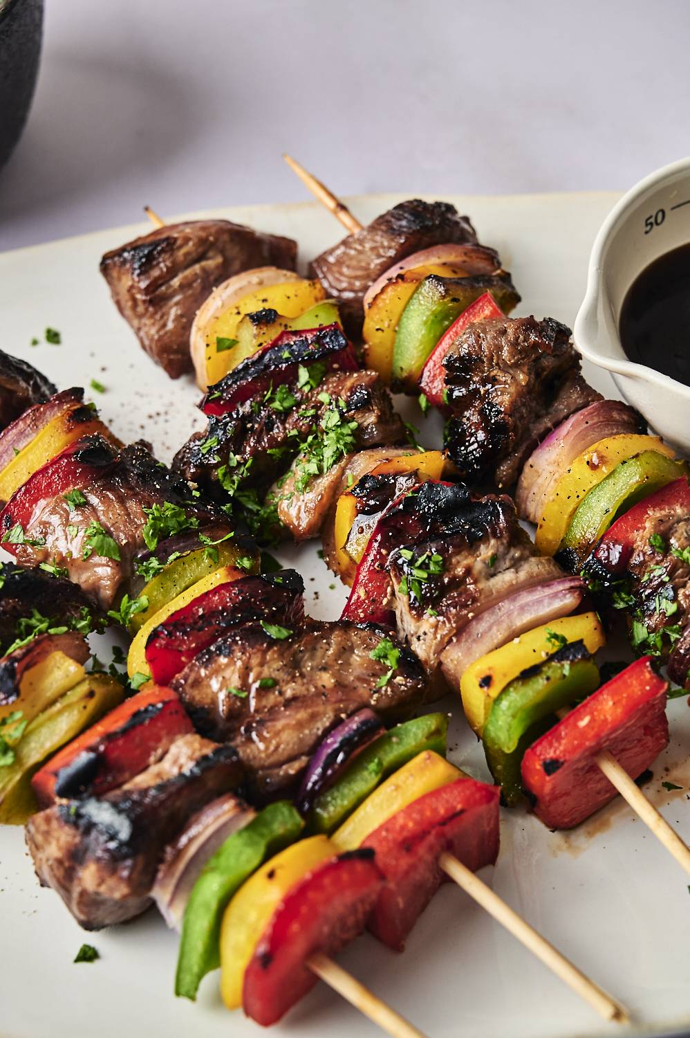Grilled beef and vegetable skewers have vibrant chili, onions, and garnish with fresh herbs with white plates.