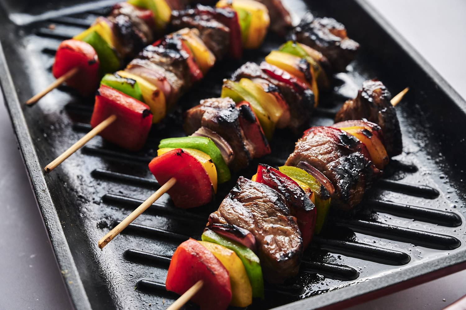 Roasted beef and colorful Bell peppers skewers sizzle on the black grill, showing off delicious summer dishes.