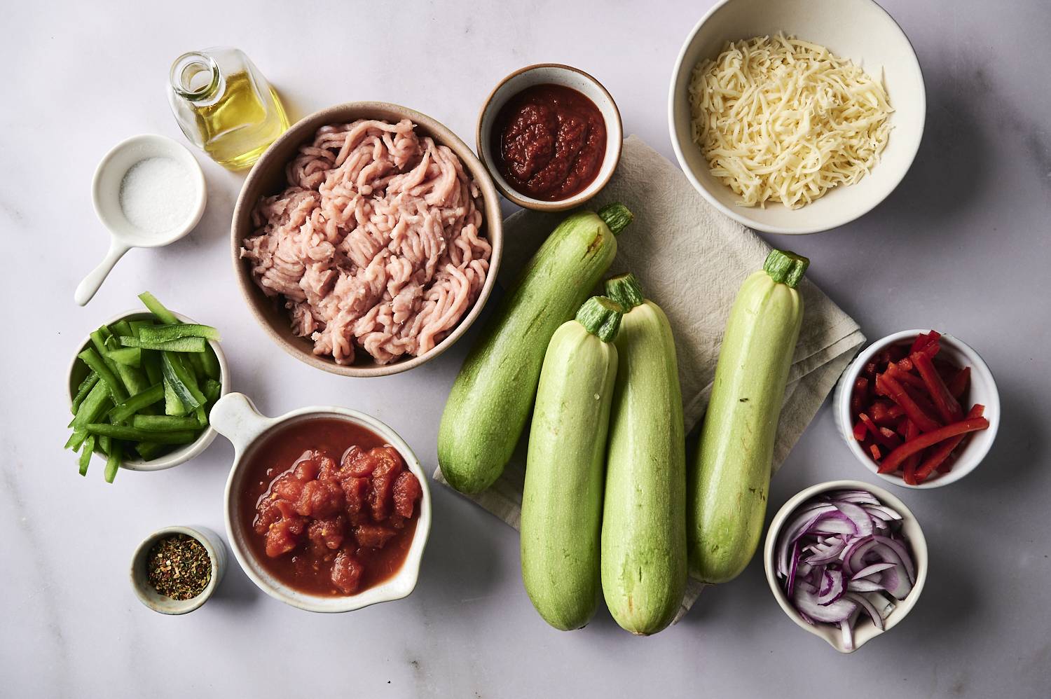 Ingredients for Tex-Mex stuffed zucchini, including zucchini, ground meat, tomato sauce, shredded cheese, and seasonings.
