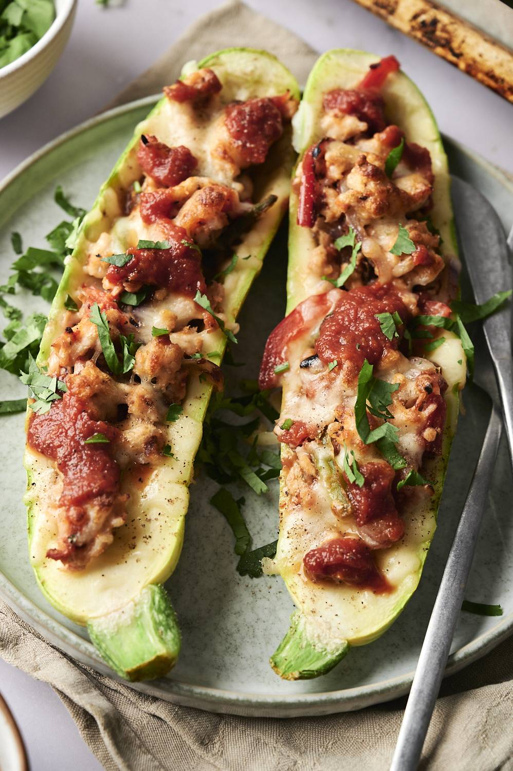 This image shows two stuffed zucchini halves, topped with a combination of melted cheese, seasoned ground turkey, and a tomato-based sauce. 