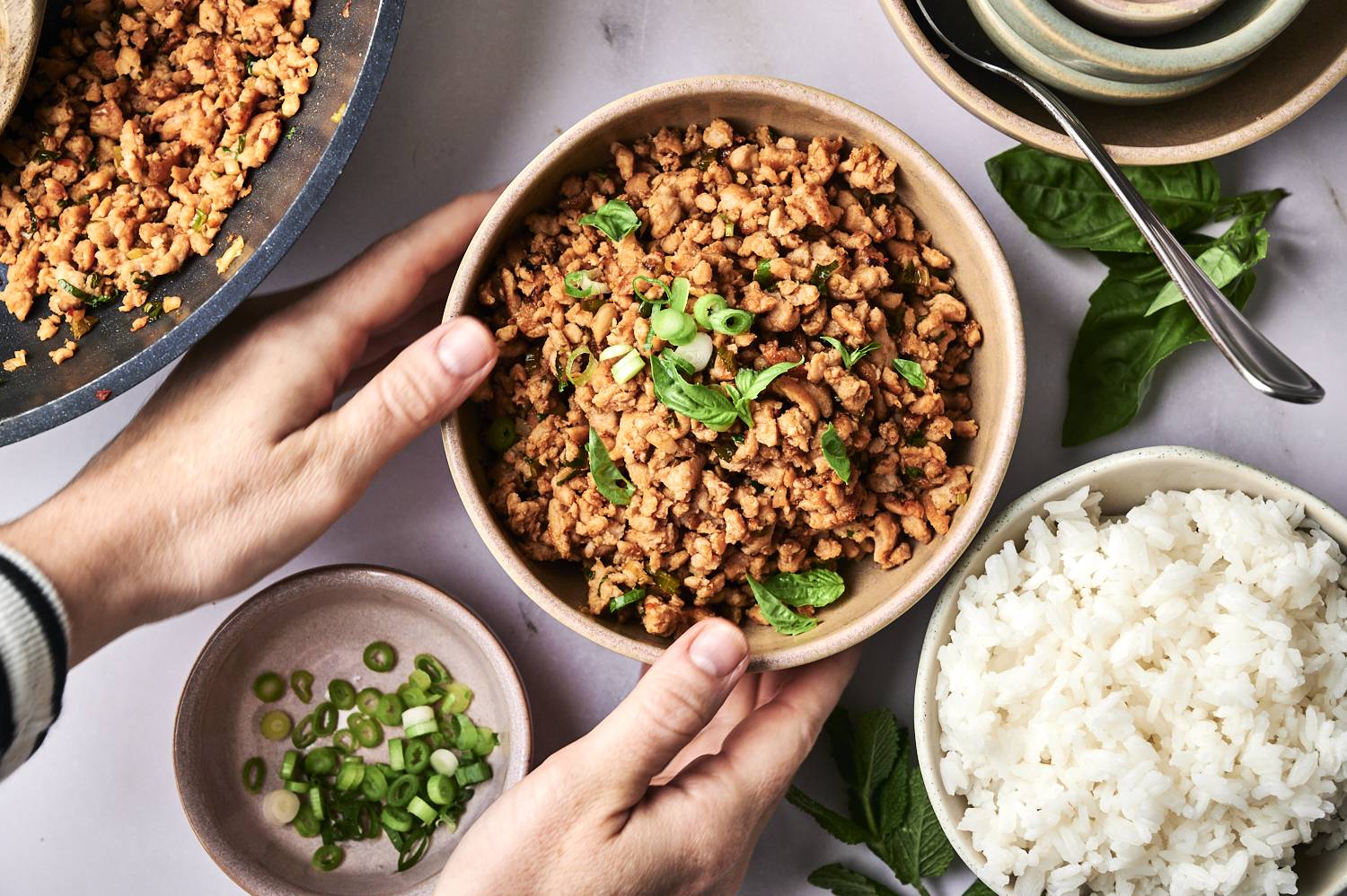 One man holds a bowl of seasoned chopped meat with green onions and basil, accompanied by rice and chopped shallots.