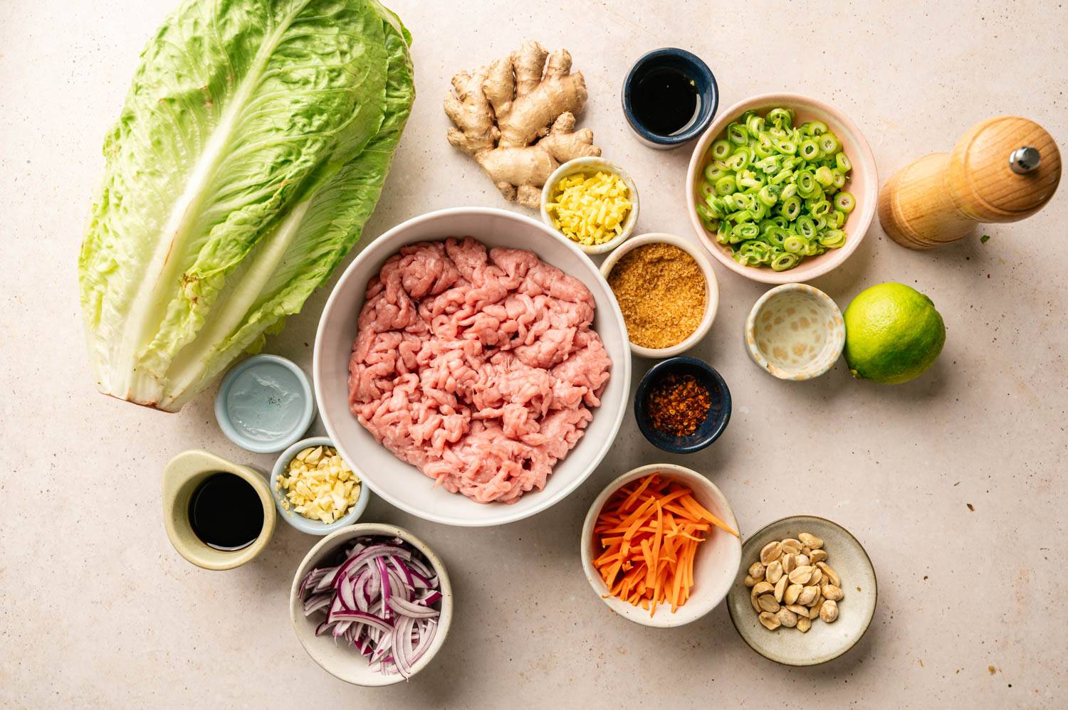 Raw ingredients for Thai turkey lettuce wraps arranged on a countertop, including ground turkey, romaine lettuce, ginger, garlic, green onions, carrots, lime, peanuts, and seasonings.