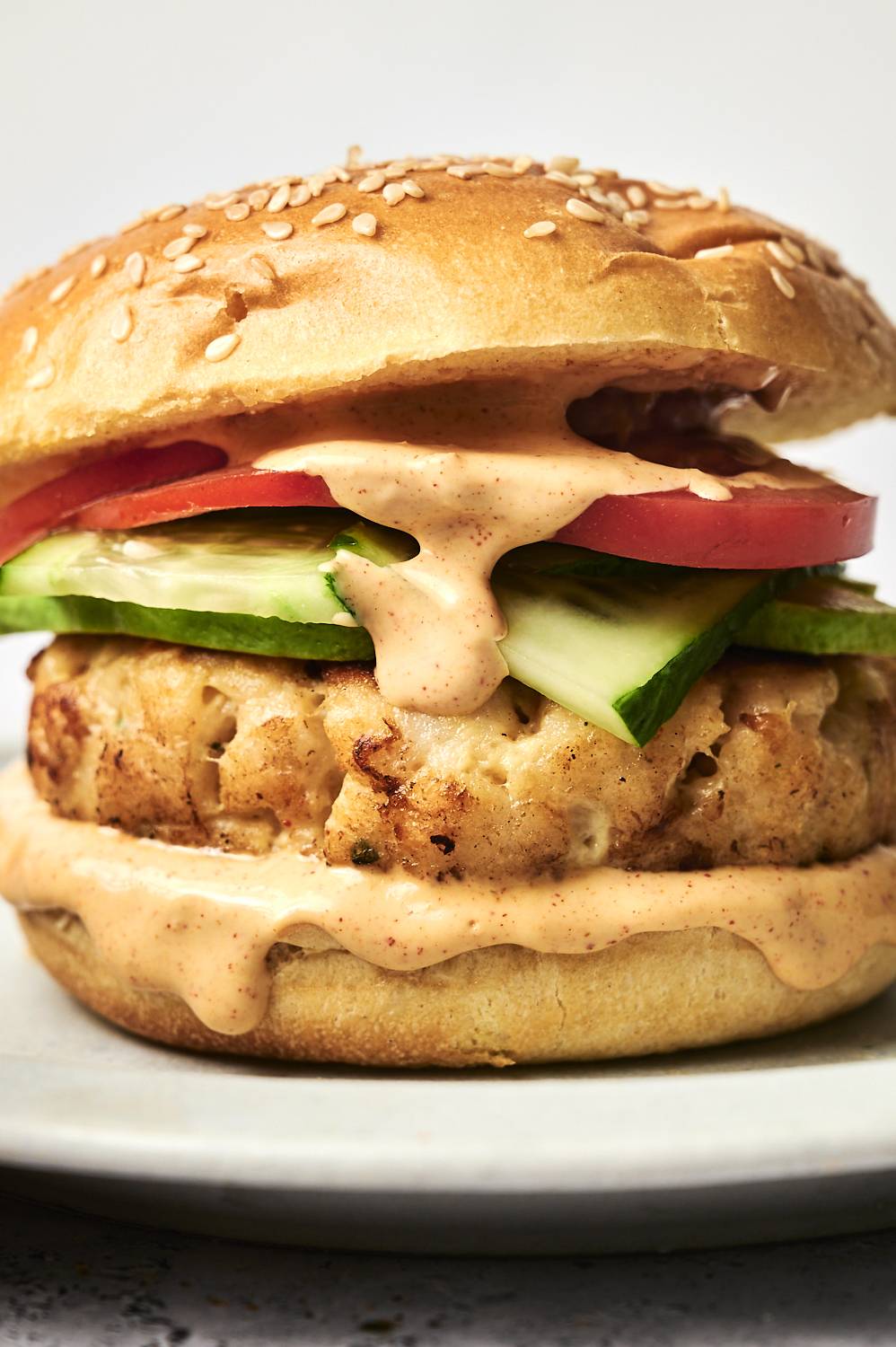 Tilapia fish burger with creamy sauce cucumber and tomato on a sesame seed bun.