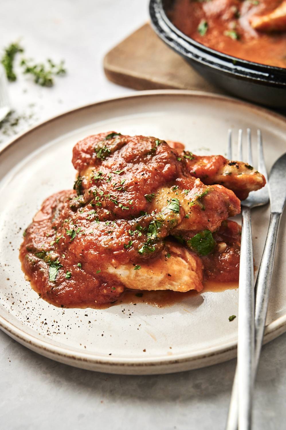 Chicken breasts with homemade tomato basil sauce served on a plate with a fork and knife.
