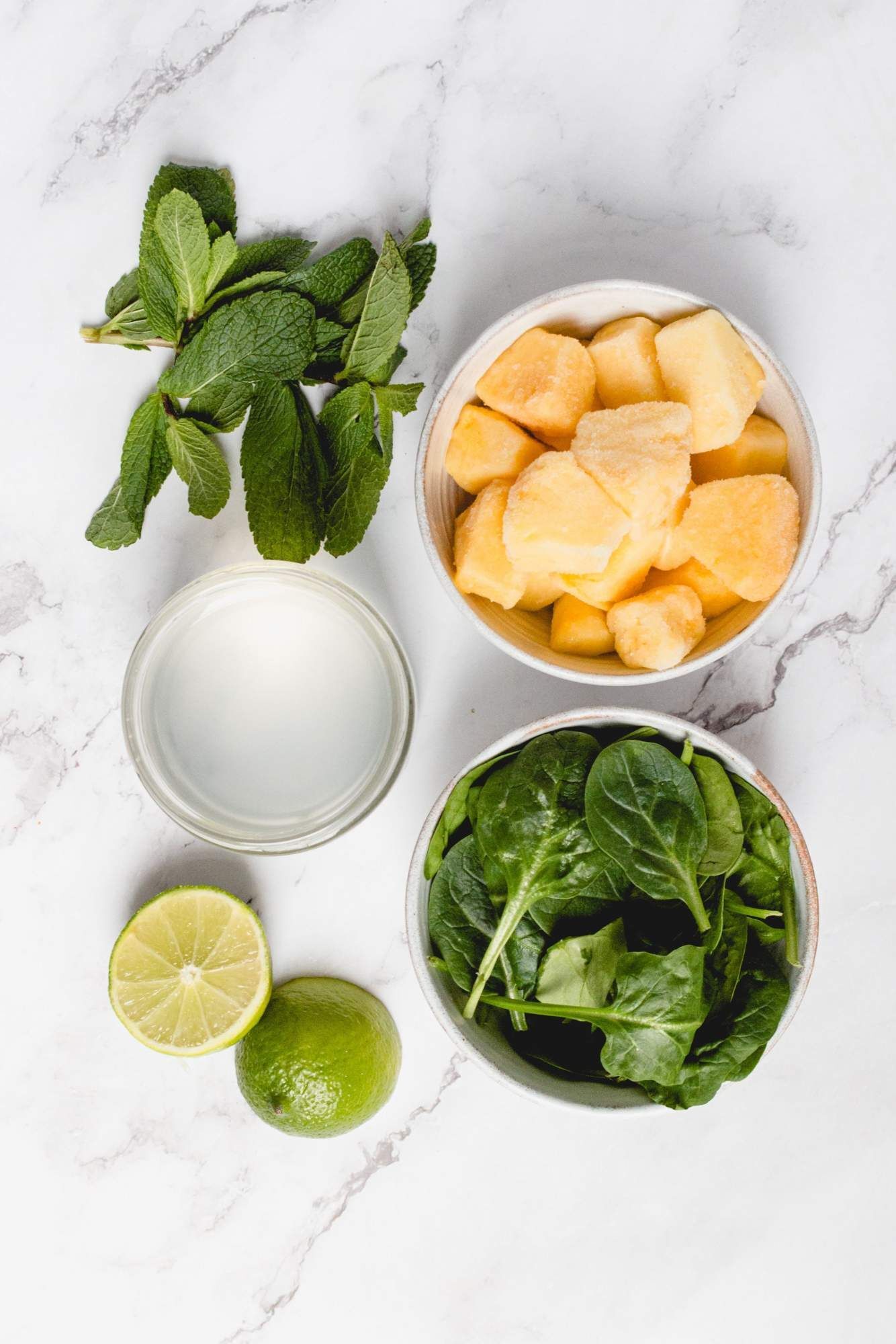 Ingredients for pineapple smoothie, including frozen pineapple, spinach, mint, lemon juice and coconut water.