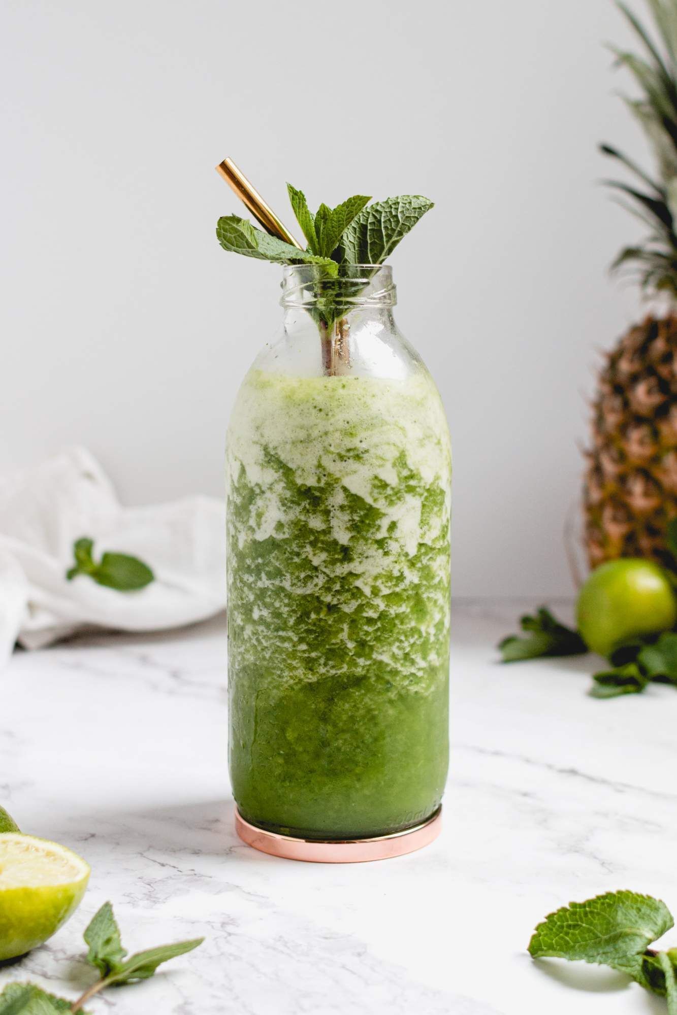 Tropical pineapple and mint mojito smoothie with mint sprigs and golden straw.