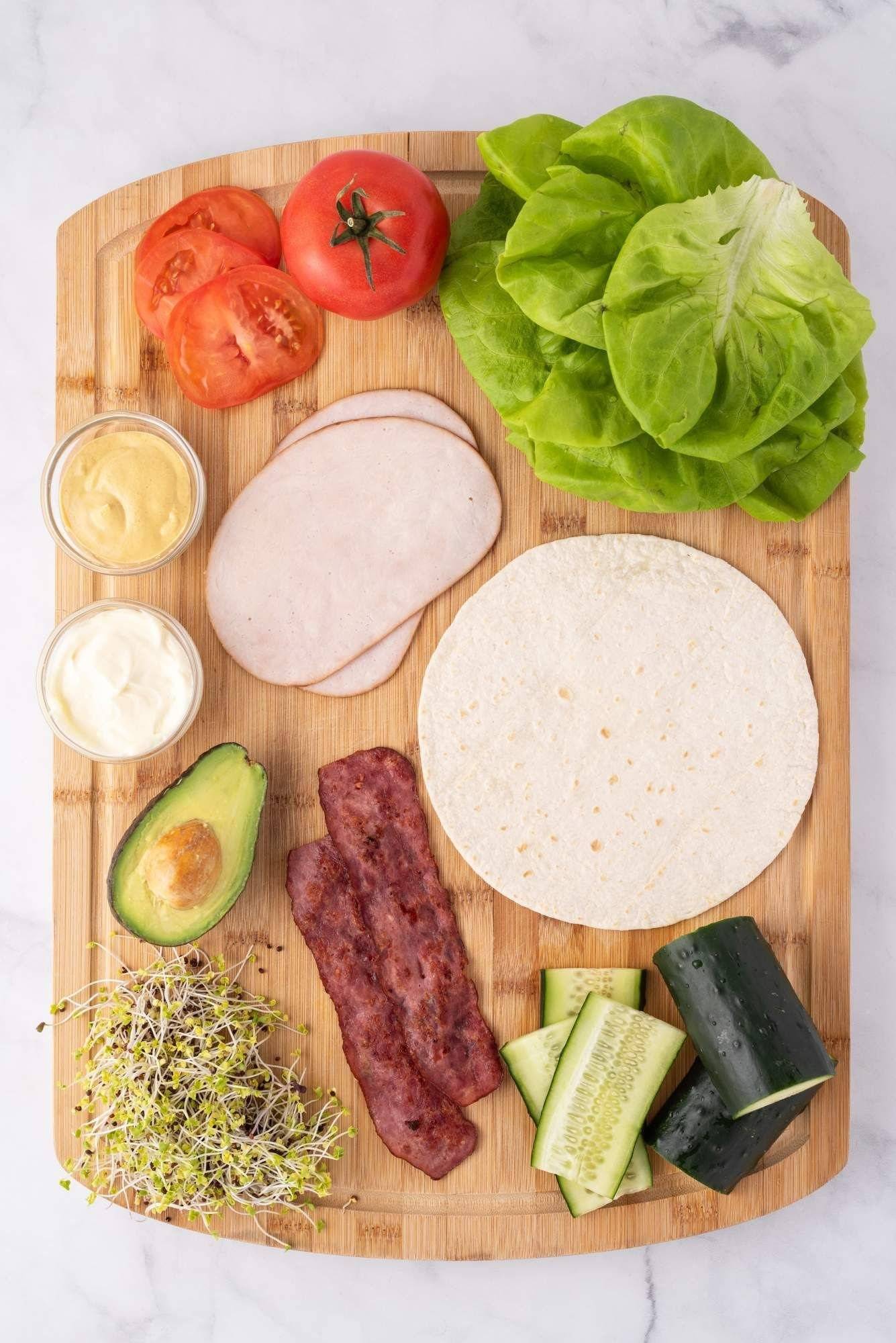 Ingredients for turkey wraps including deli turkey, bacon, avocado, wrap, veggies and sauce.