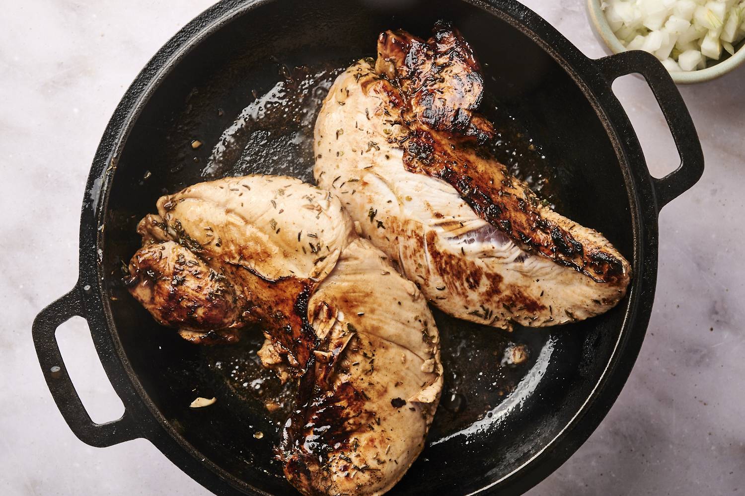 Two turkey tenderloins being seared in a cast iron skillet.