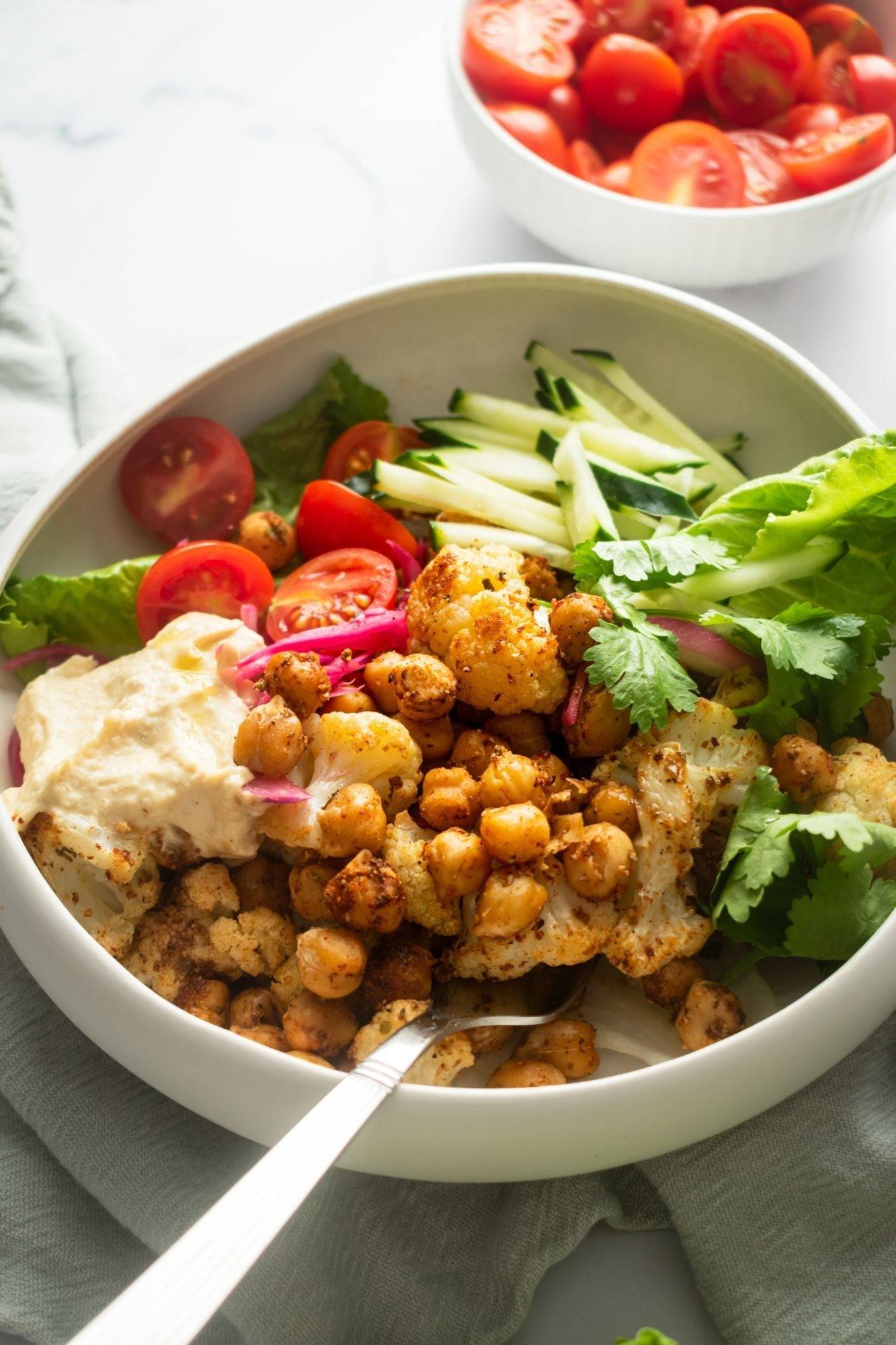 Chickpea shawarma bowl with cauliflower, cucumber, tomato, lettuce and hummus in a white bowl.