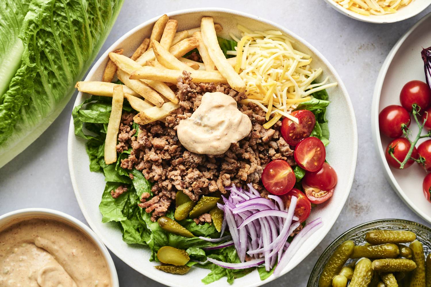 Burger bowls with lettuce, ground beef, fries, tomatoes, cheese, pickles, and thousand island dressing.