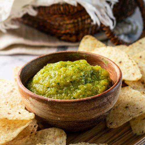 Delicious Mexican salsa verde served on a wooden bowl accompanied by crispy tortilla chips.