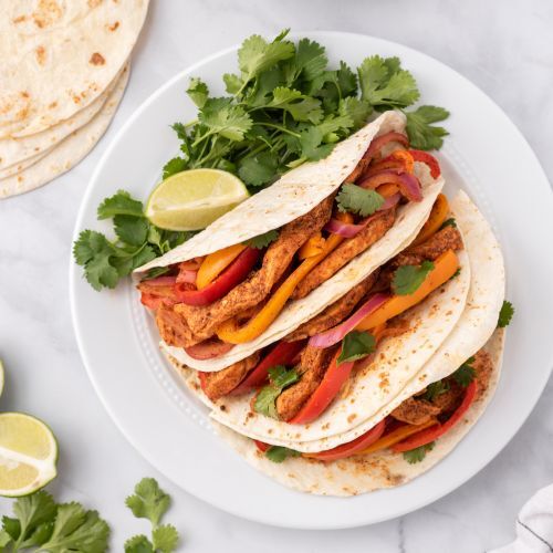 Chicken fajitas with peppers, onions, and cilantro in flour tortillas.