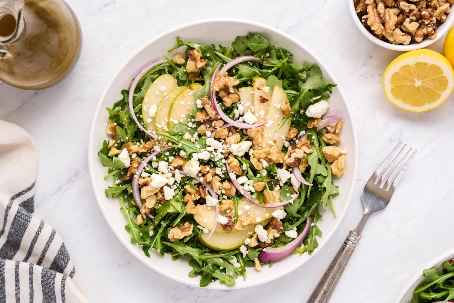 Easy Arugula Salad Arugula salad with sliced pears, toasted walnuts, red onions, goat cheese, and vinaigrette tossed in a ceramic bowl.