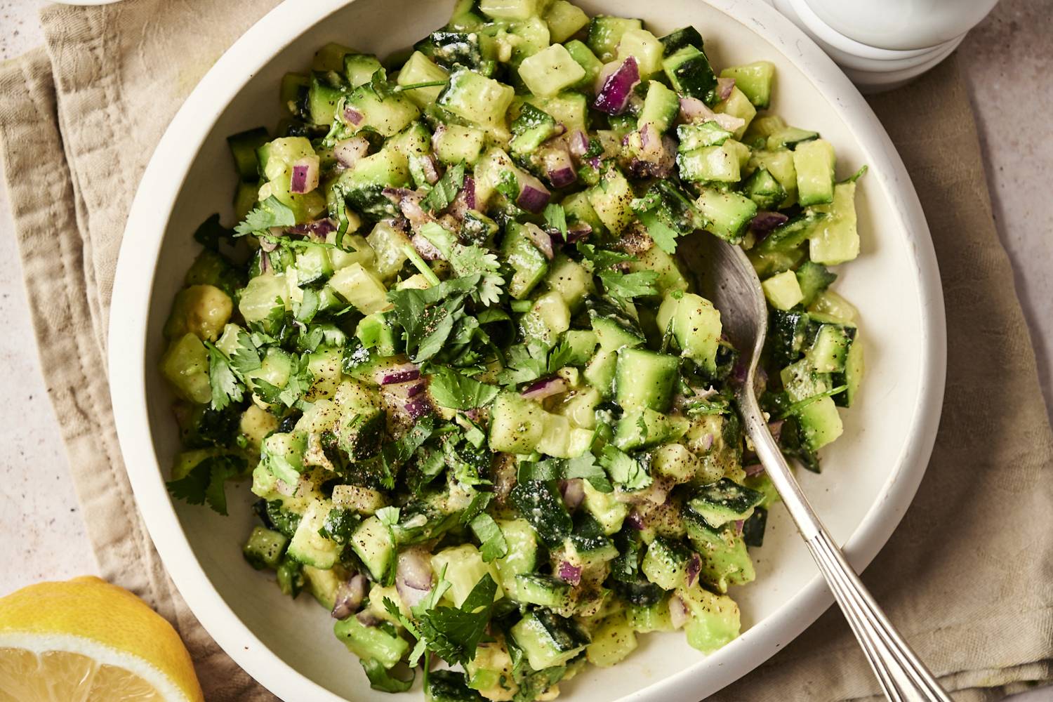 Avocado Cucumber Salsa Close-up of avocado cucumber salsa in a white bowl, garnished with fresh cilantro and black pepper, with a spoon ready for serving.