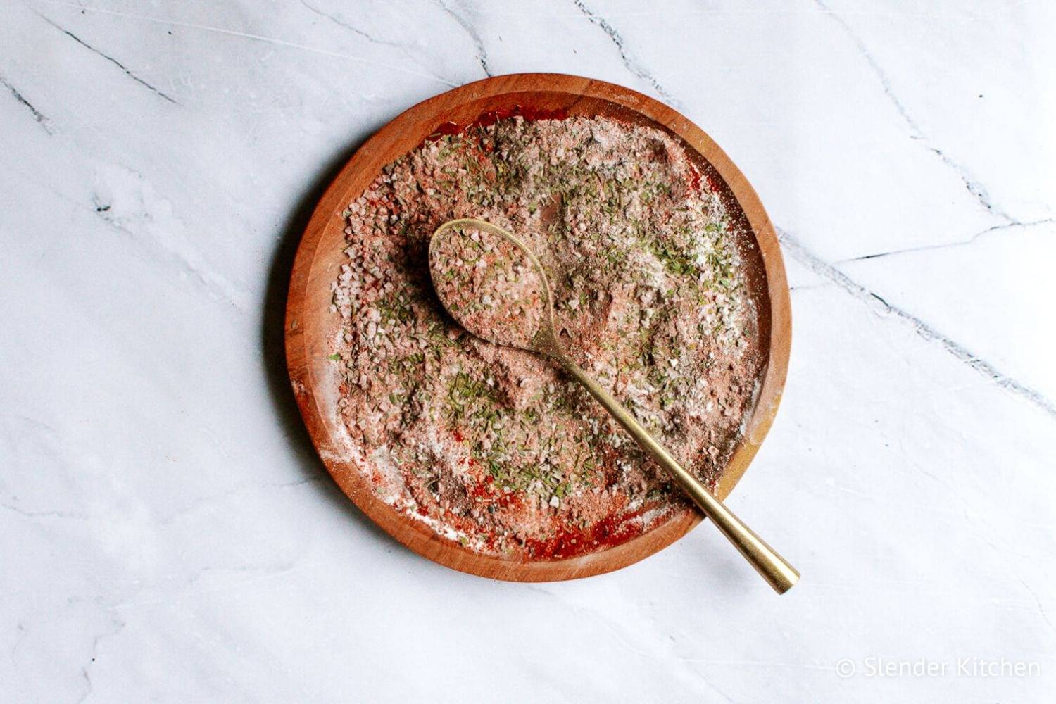 18 Must Try Seasonings and Marinades for Grilled Vegetables Cajun seasoning blend with smoked paprika, garlic powder, onion powder, oregano, and thyme on a wooden plate with a gold spoon.