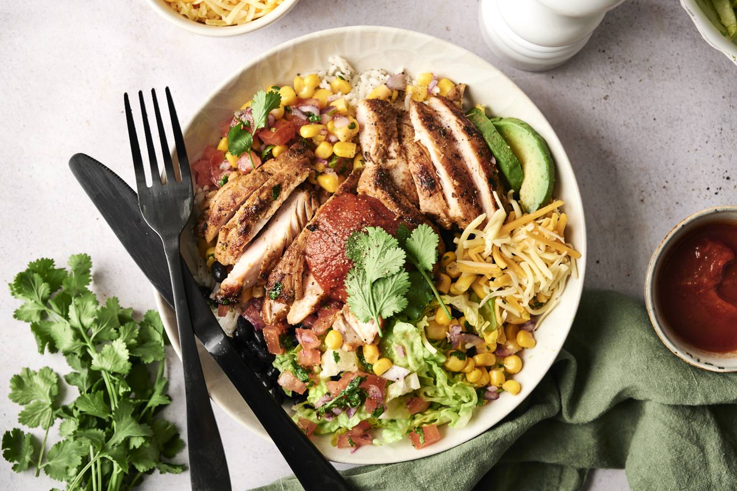 Chipotle Chicken Burrito Bowl A colorful bowl featuring grilled chicken slices, corn, cheese, lettuce, and salsa, garnished with cilantro and avocado.