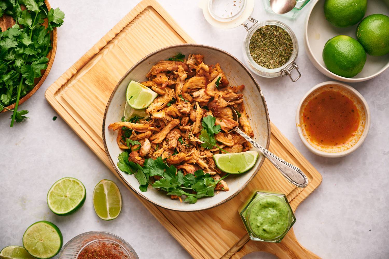 38 Low Carb Mexican Recipes Chicken carnitas in a bowl sitting on a wooden cutting board with ingredients around it.