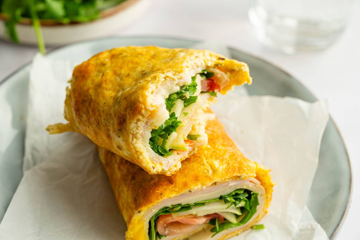Cottage cheese flatbread wrap filled with turkey, sharp cheddar, arugula, tomato, and thinly sliced green apple, sliced in half and stacked on parchment paper.