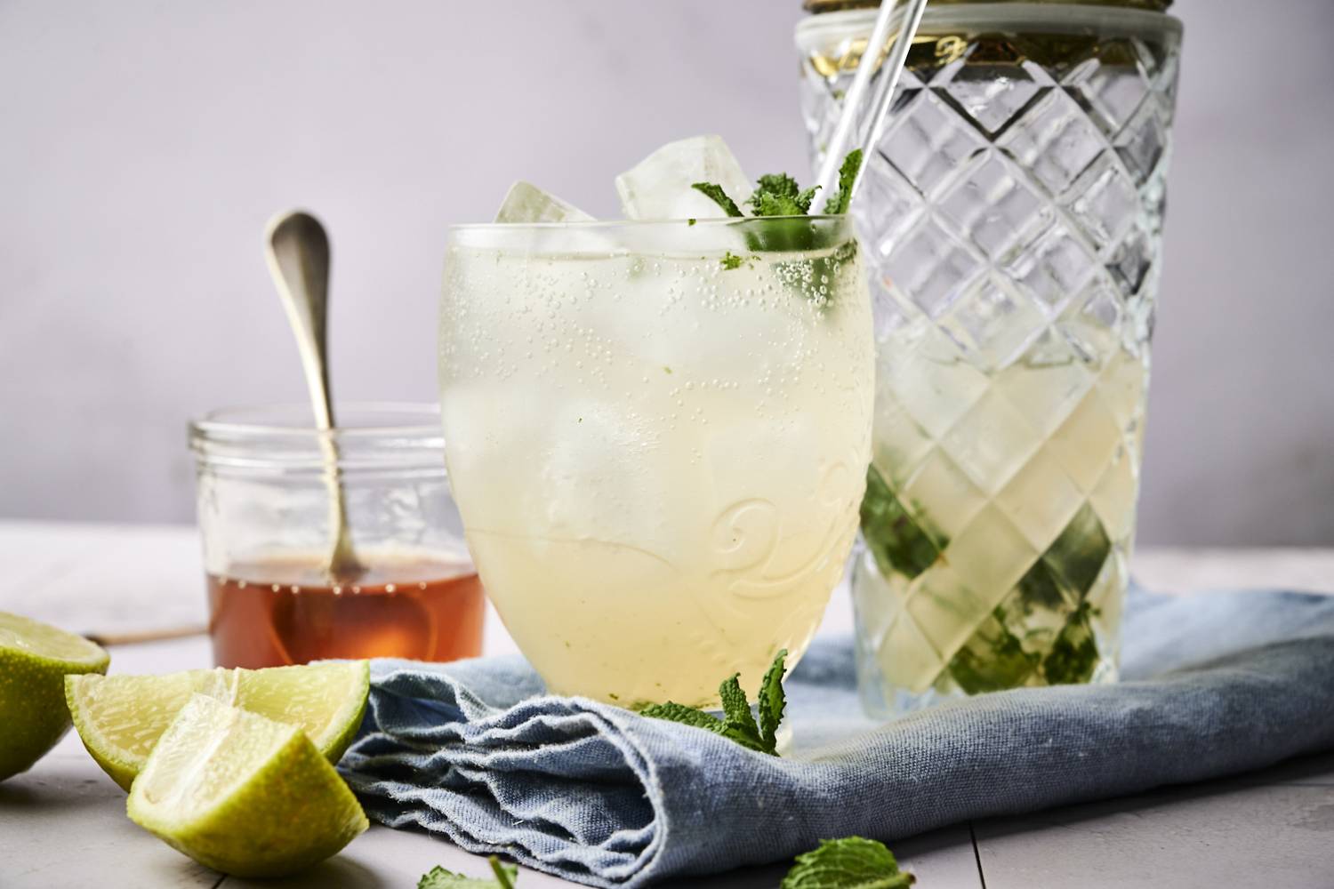 Easy Mojitos A refreshing drink with mint and ice, next to a jar of honey and lime wedges on a blue napkin.