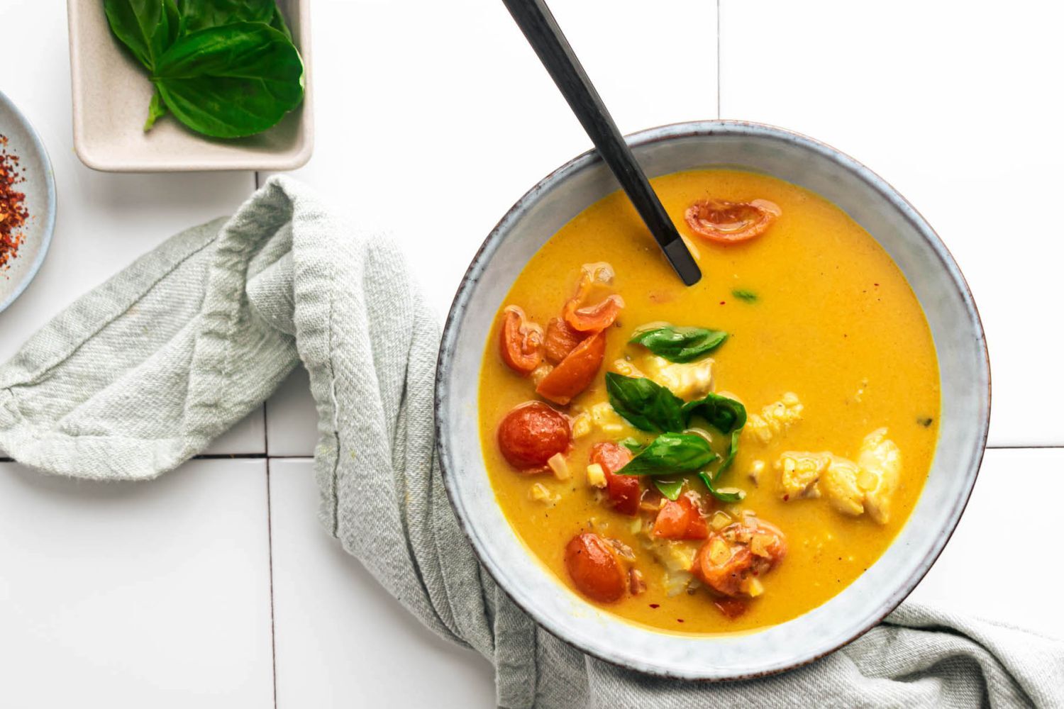 Fish Curry Fish curry with cooked cod, coconut broth, curry seasoning, garlic, ginger, and basil in a bowl with tomatoes.