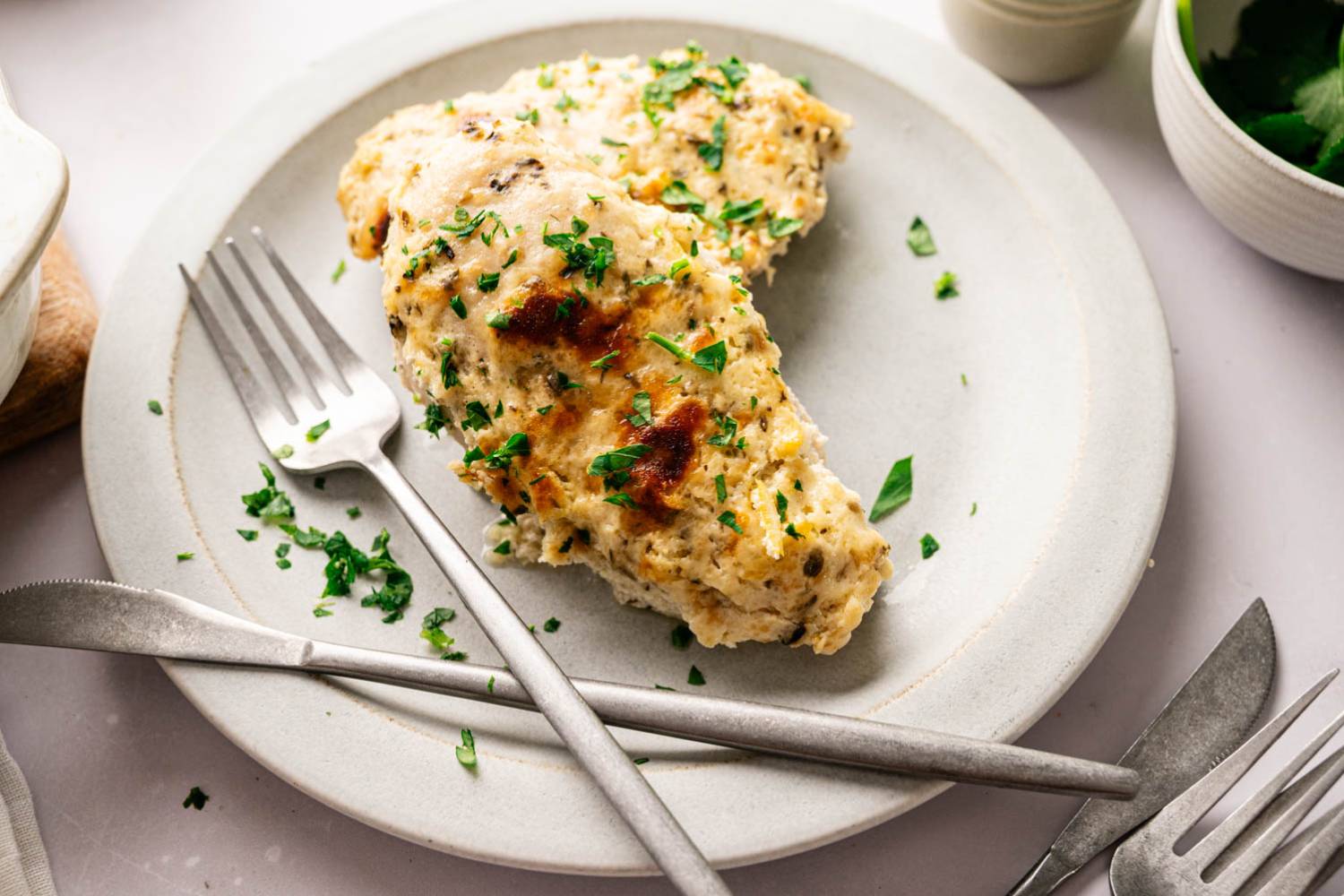 Creamy baked Parmesan chicken breasts in a casserole dish, garnished with chopped parsley.