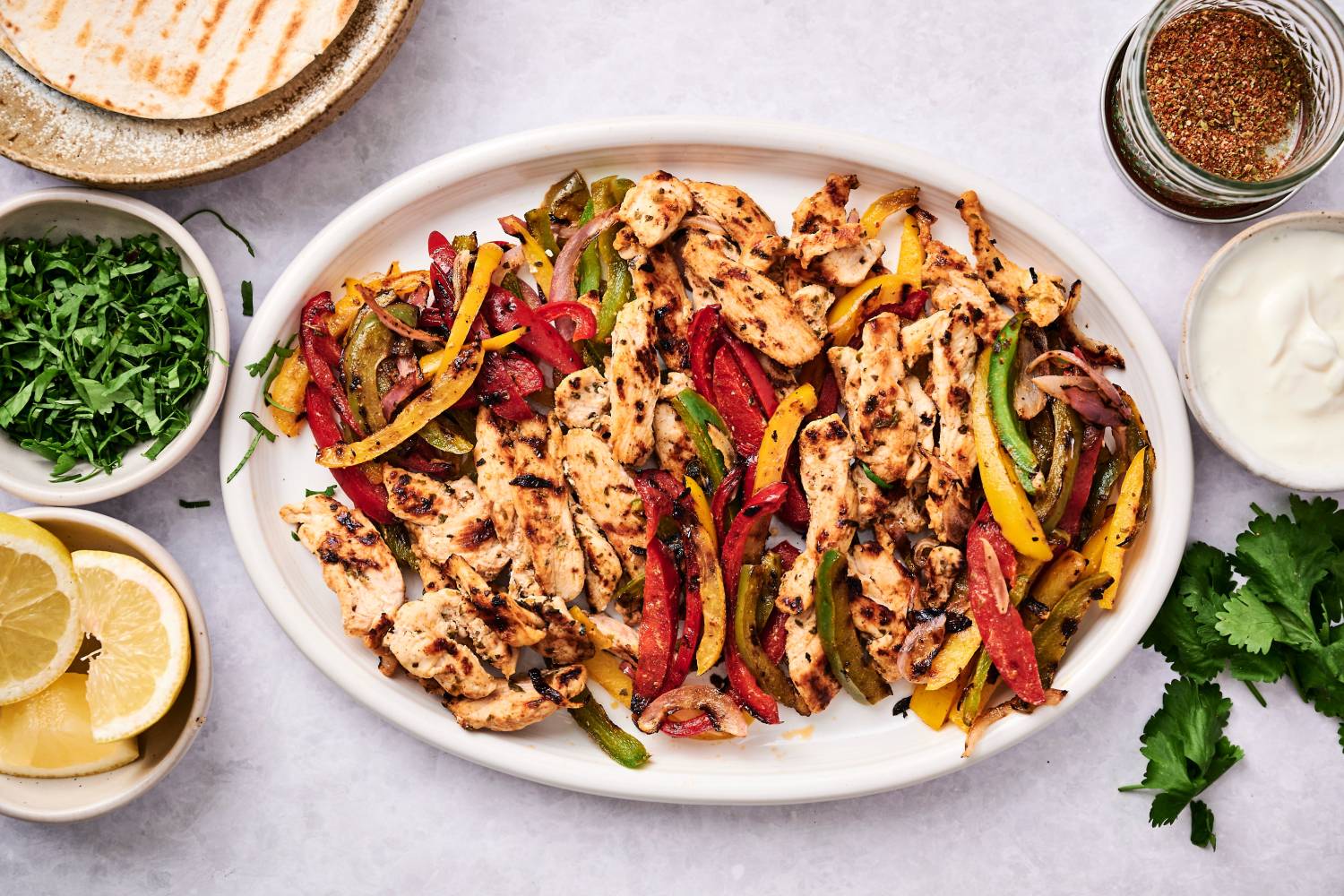 Grilled chicken fajitas with bell peppers and onions on a platter with fresh cilantro, salsa, sour cream, and tortillas.