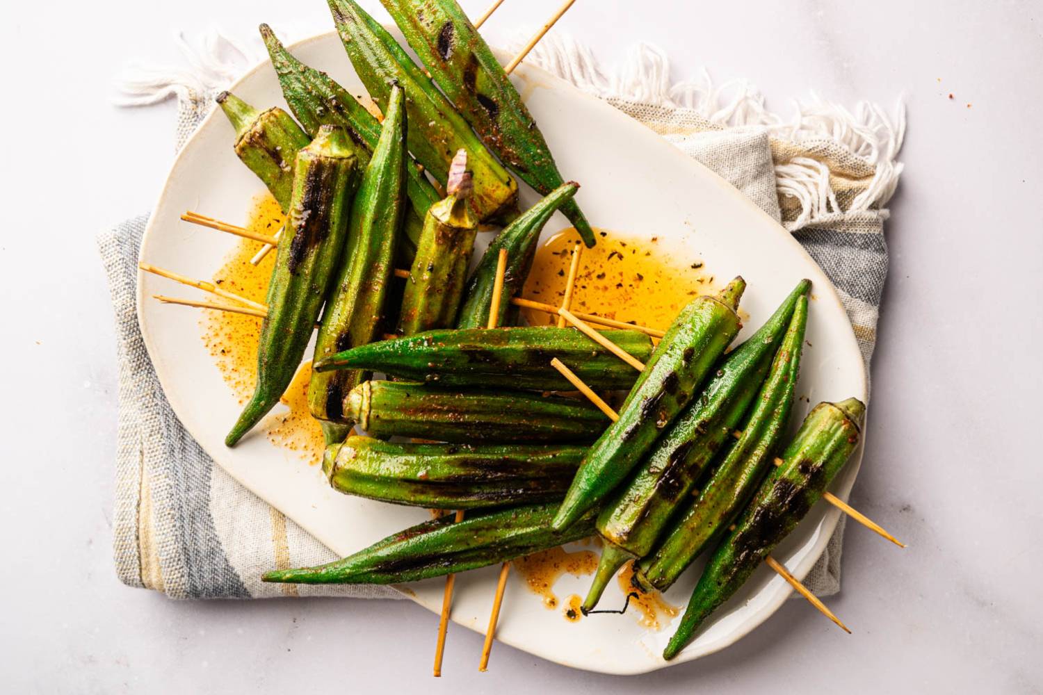 Best Grilled Okra Recipe Grilled okra skewers arranged on a serving platter with smoky char marks and a sprinkle of Cajun seasoning.