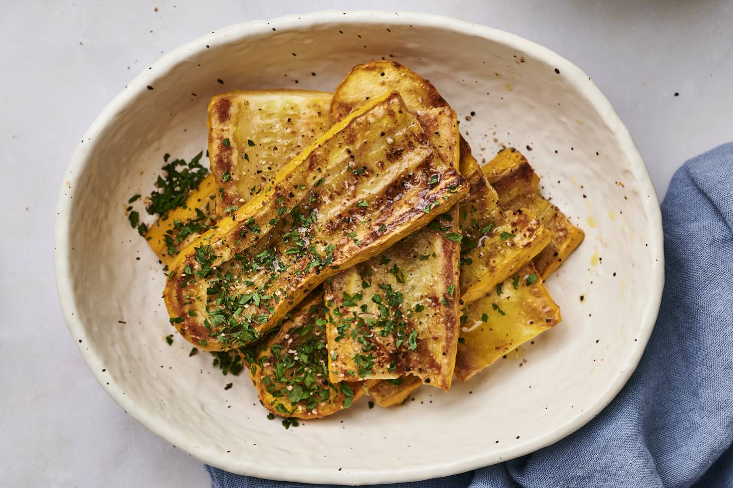 Grilled Yellow Squash Grilled yellow squash on a black plate sprinkled with parsley.
