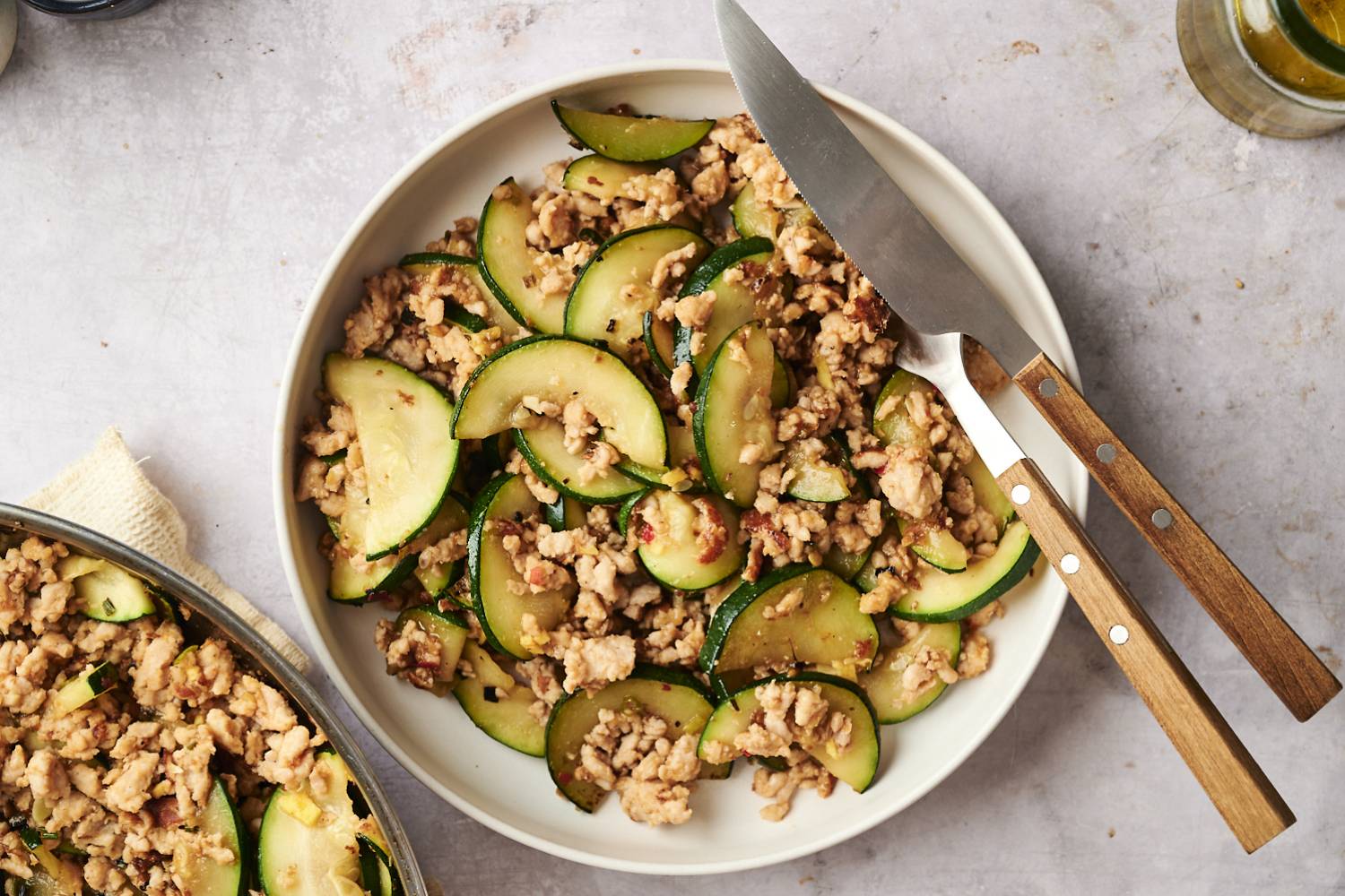 Ground Turkey and Zucchini Stir Fry Bowl of ground turkey zucchini stir fry with tender zucchini slices and browned turkey, served with a knife and fork on the side.