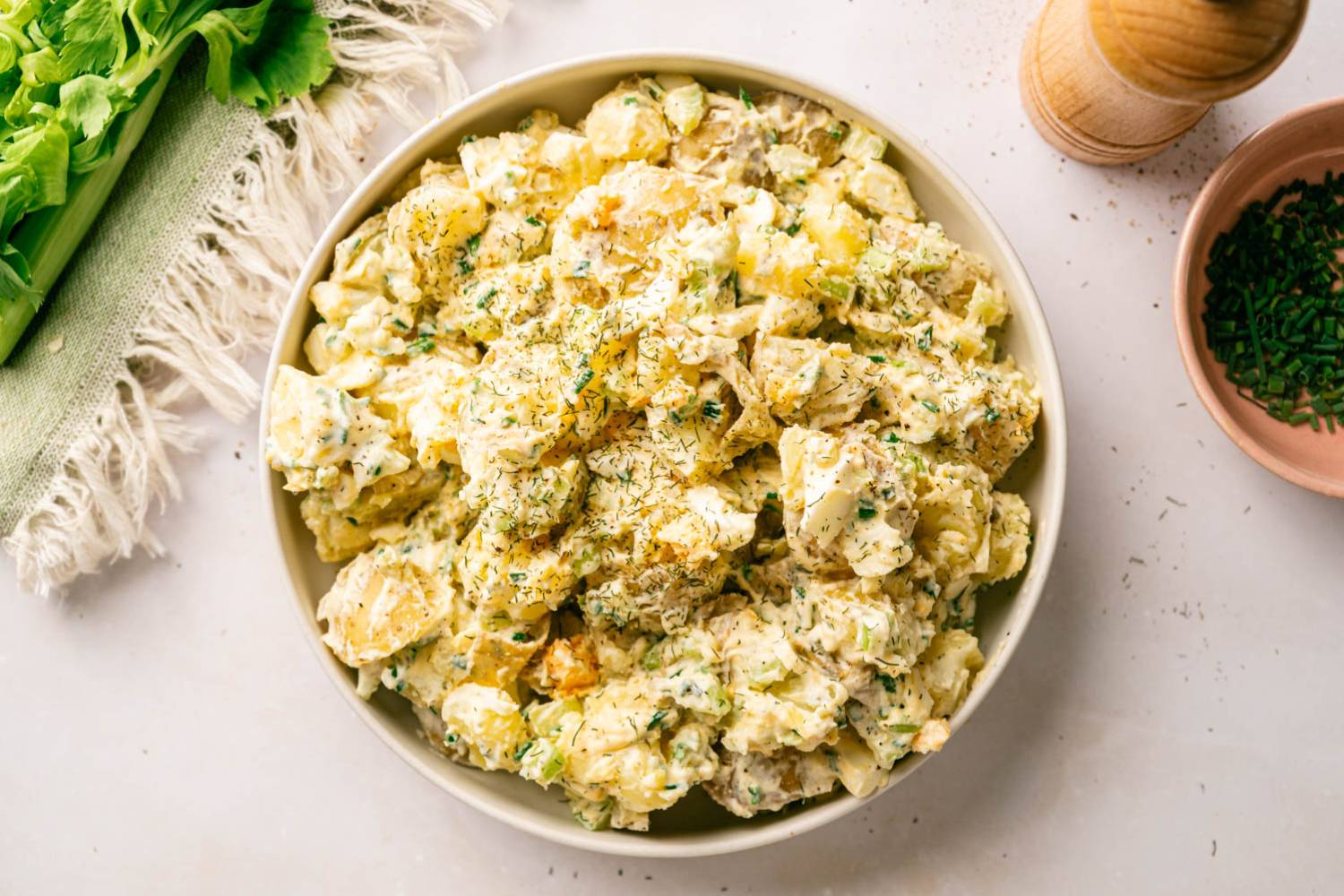 Healthy Potato Salad Close-up of chunky potato salad garnished with dill and chives, served in a wide bowl on a green striped napkin.