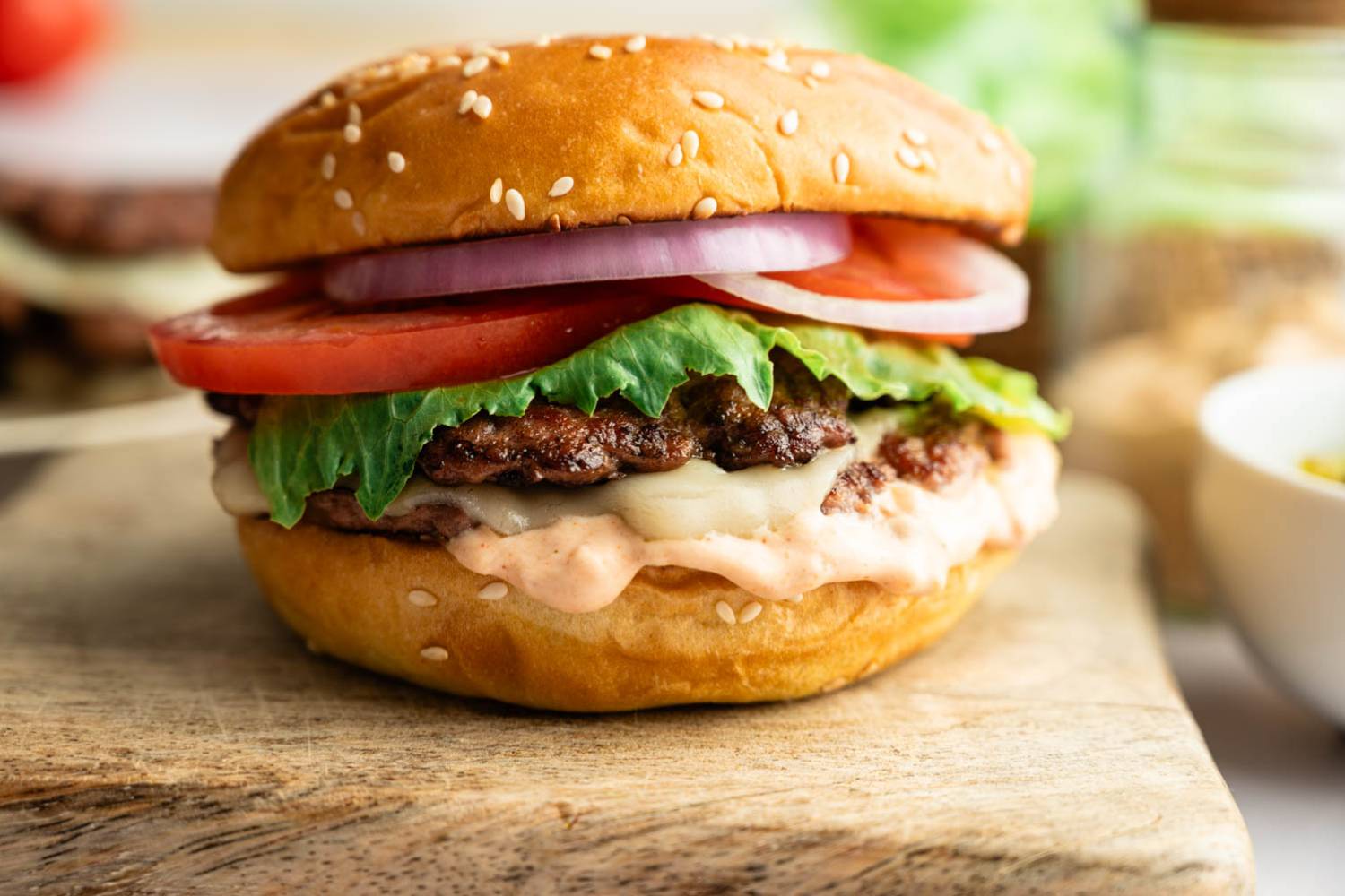 Healthy Smash Burger Side view of a homemade smash burger with melted cheese, crisp lettuce, sliced tomato, red onion, and burger sauce on a toasted brioche bun.