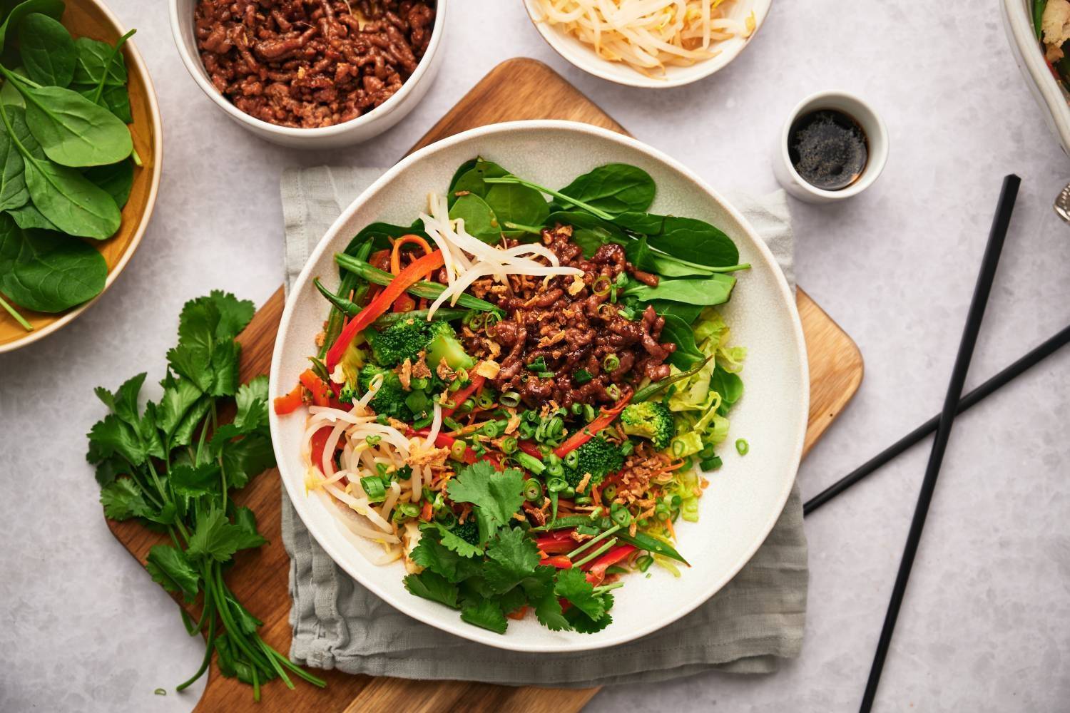 25+ Macro-Friendly Recipes That Taste Amazing Korean beef bowls with rice, cilantro, carrots, bell peppers, and sprouts in a bowl with spicy sauce.
