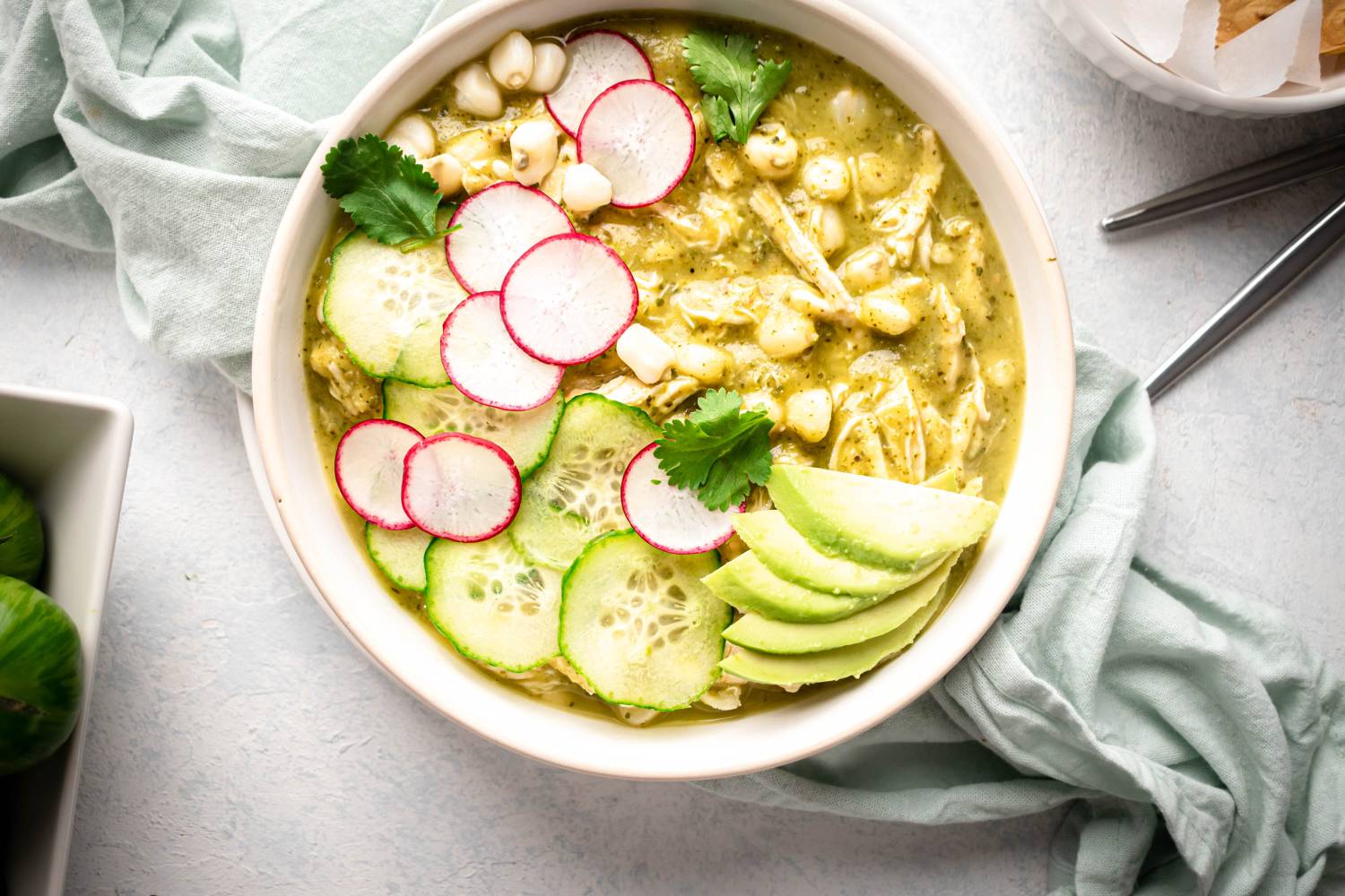 Mexican Soup Green chicken pozole in a bowl with avocado, radish, cilantro, chicken, and hominy.