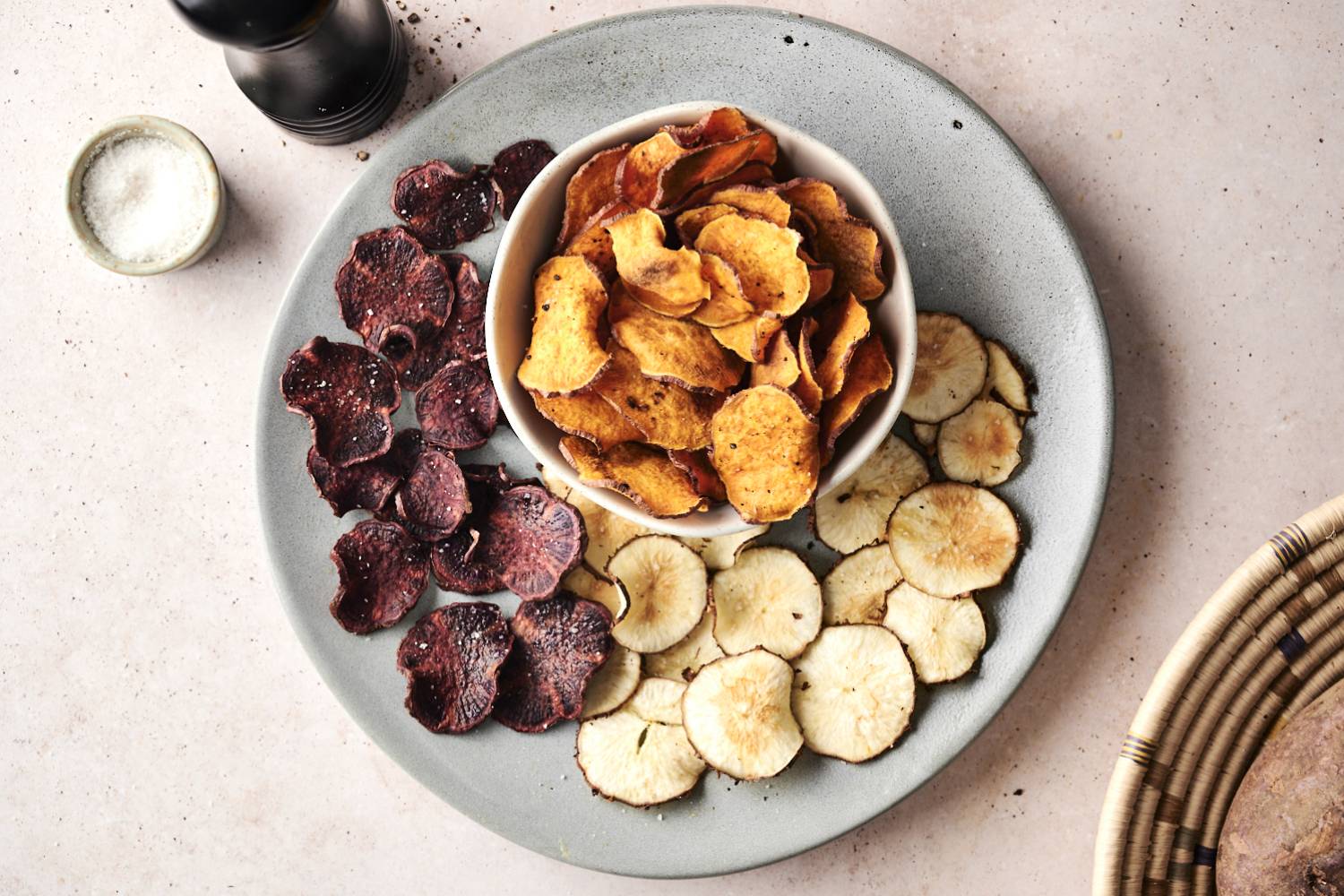 Microwave Veggie Chips A platter of assorted vegetable chips in three colors: purple, golden, and white, served alongside a small bowl of salt.