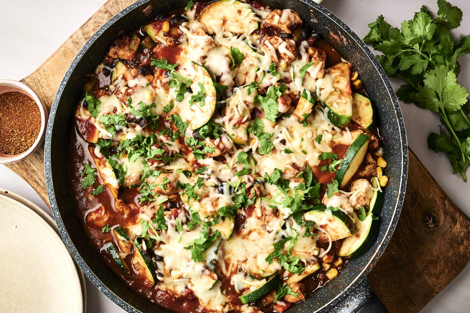 One Pot Mexican Chicken and Zucchini  A skillet of cheesy chicken, black beans, and zucchini is served on plates, garnished with fresh cilantro and spices.