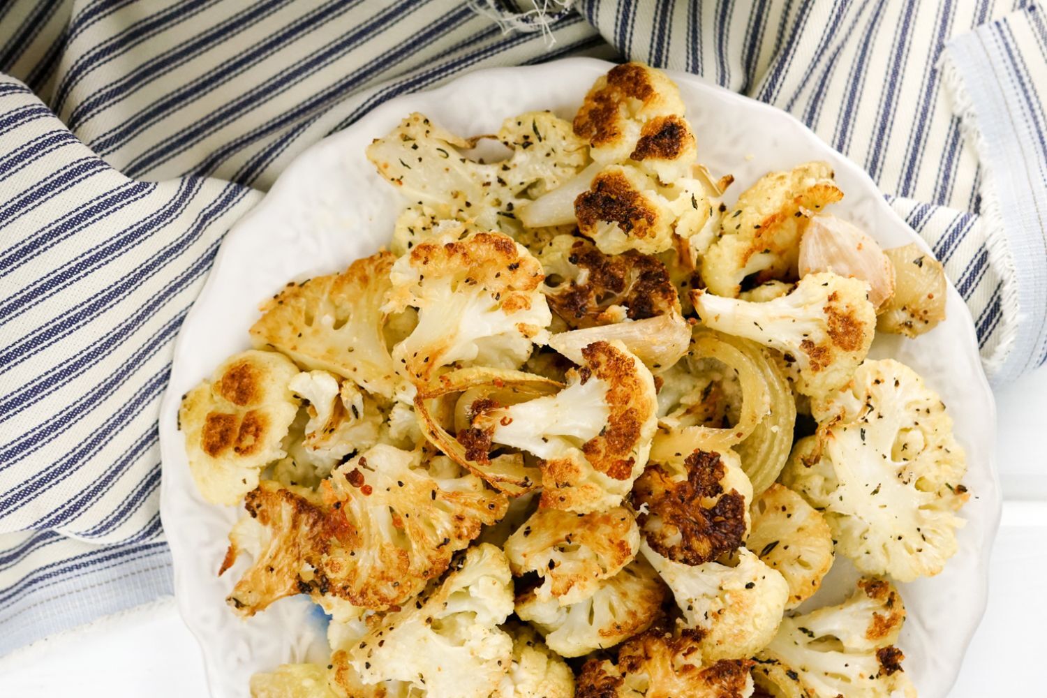 Parmesan Roasted Cauliflower Parmesan Roasted Cauliflower with garlic cloves, parsley, and Parmesan cheese on a white plate.