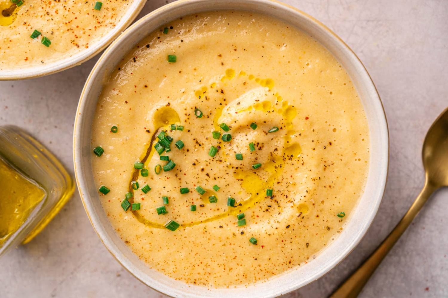 A creamy bowl of potato soup garnished with chopped chives and a drizzle of olive oil, with a sprinkle of black pepper. 