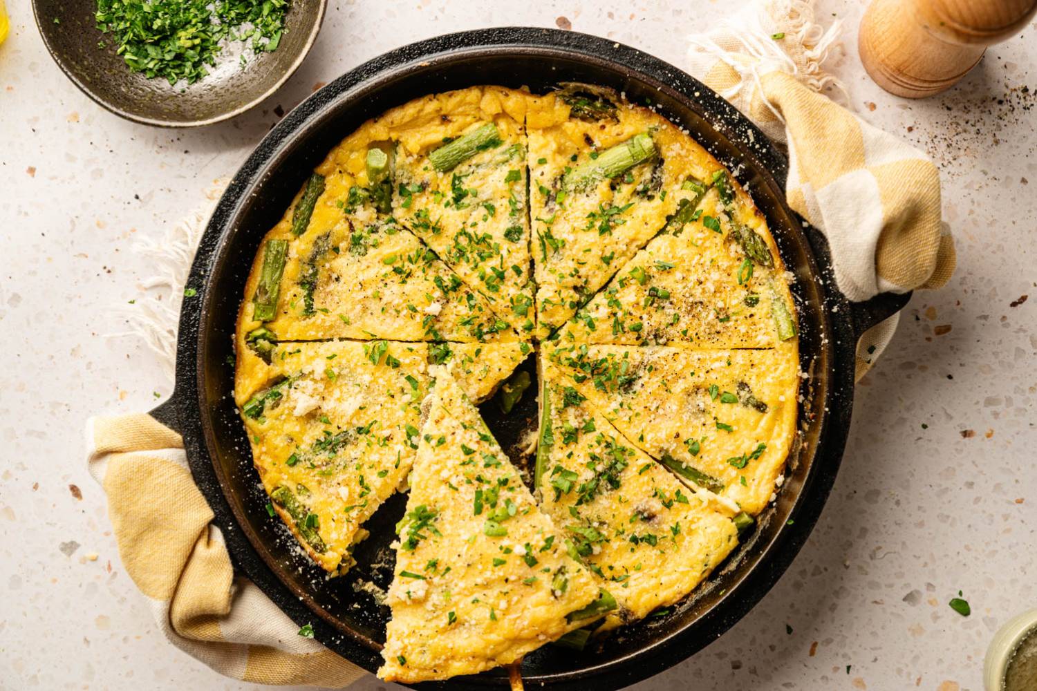 Spring Asparagus Frittata A freshly baked frittata with asparagus and herbs, sliced into wedges in a cast iron skillet.