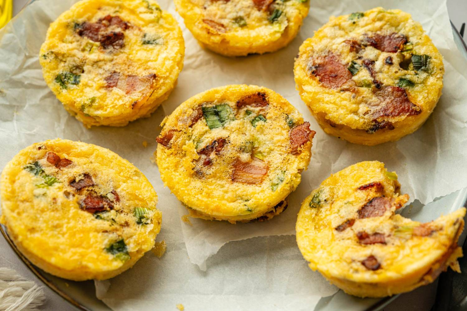 Starbucks Copycat High Protein Egg Bites Homemade high-protein egg bites arranged on a parchment-lined plate, featuring a fluffy texture with visible bacon and green onion pieces.