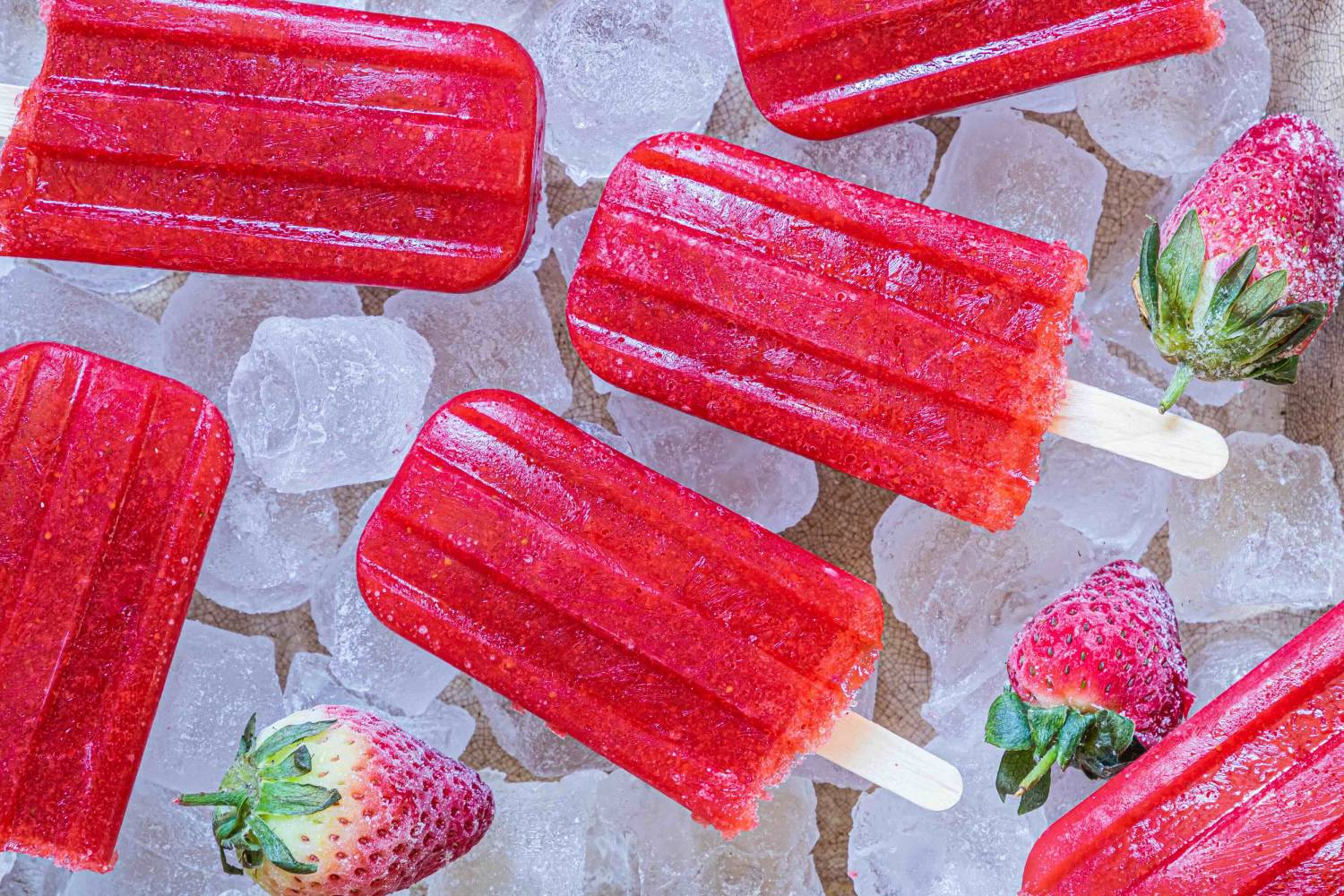 Strawberry Popsicles Bright red strawberry popsicles on ice, accompanied by fresh strawberries, create a refreshing summer treat scene.