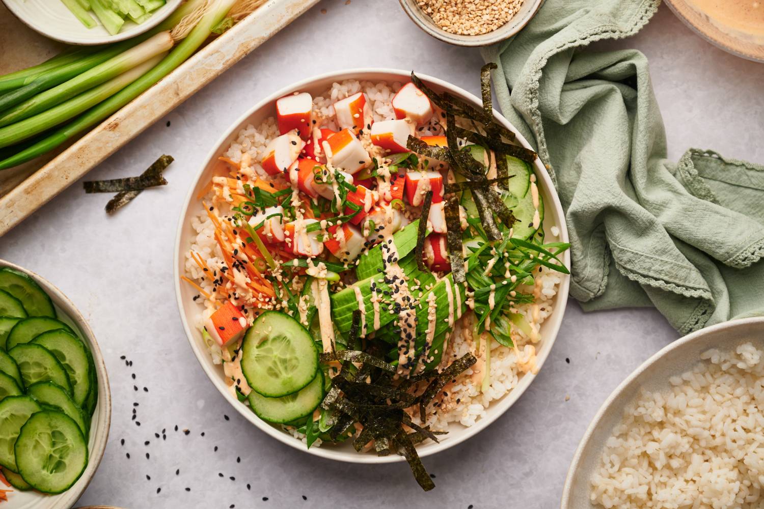 Easy Sushi Bowls (Build Your Own) Sushi bowl with imitation crab, sushi rice, nori seaweed strips, cucumbers, carrots, and spicy mayo in a white bowl.