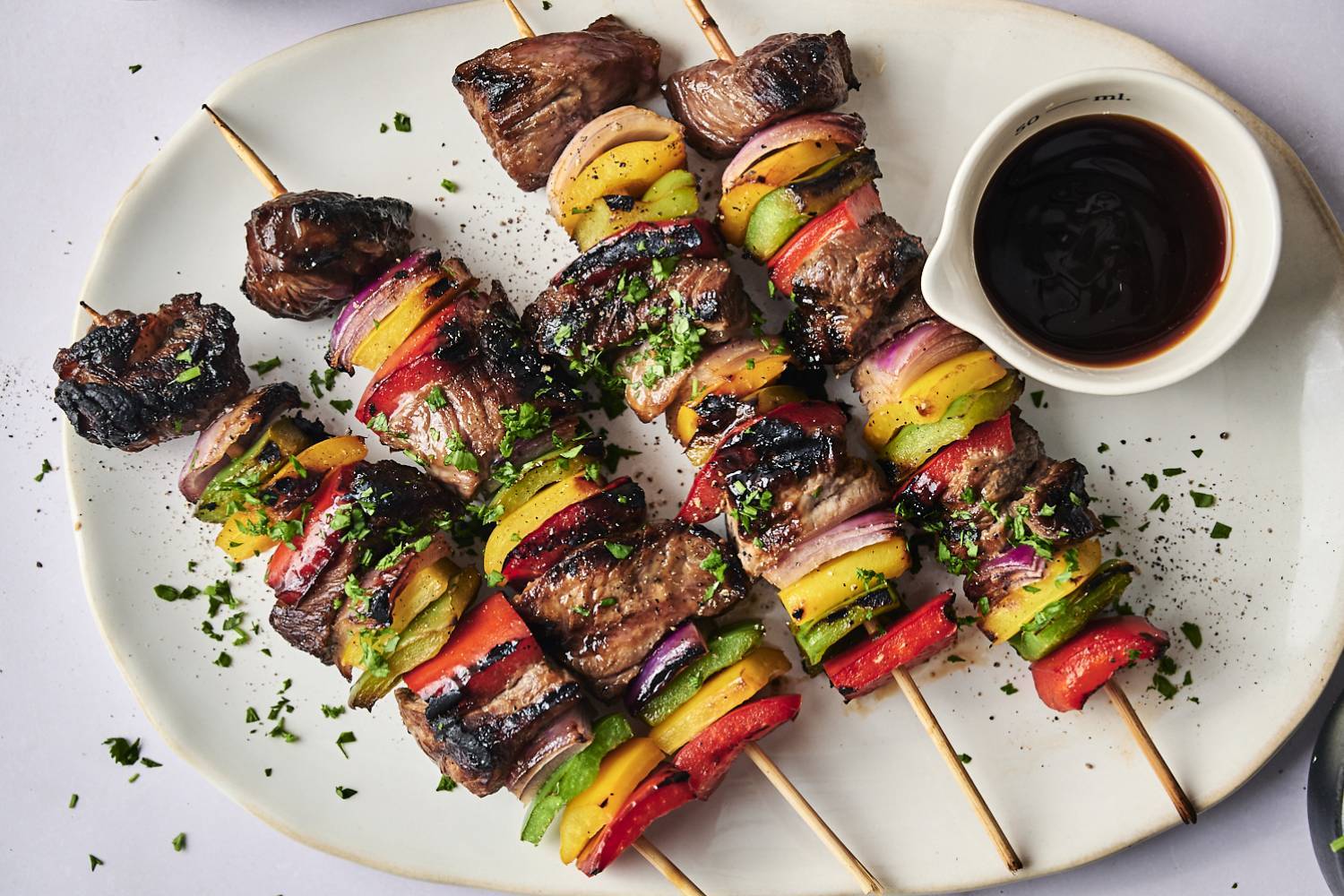 Easy Healthy Summer Recipes Grilled kebabs featuring marinated beef and colorful vegetables, served with a small bowl of dipping sauce on a white plate.