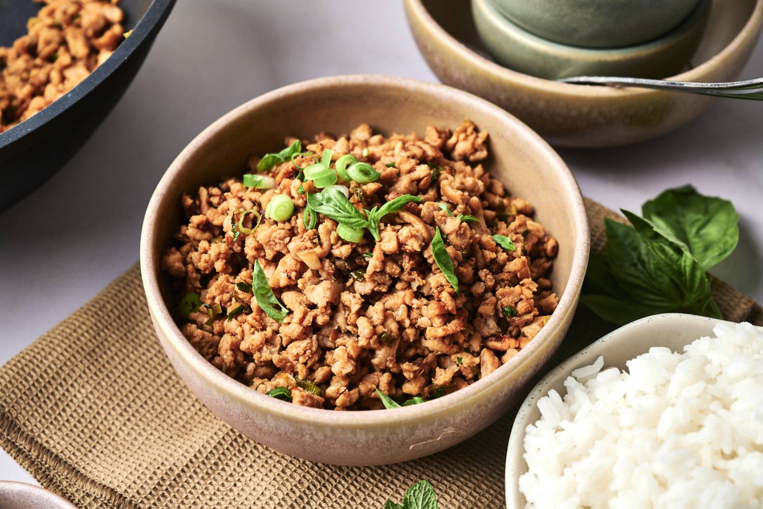 Thai Chicken Larb A bowl of seasoned ground meat topped with green onions and basil, served alongside a side of fluffy white rice.