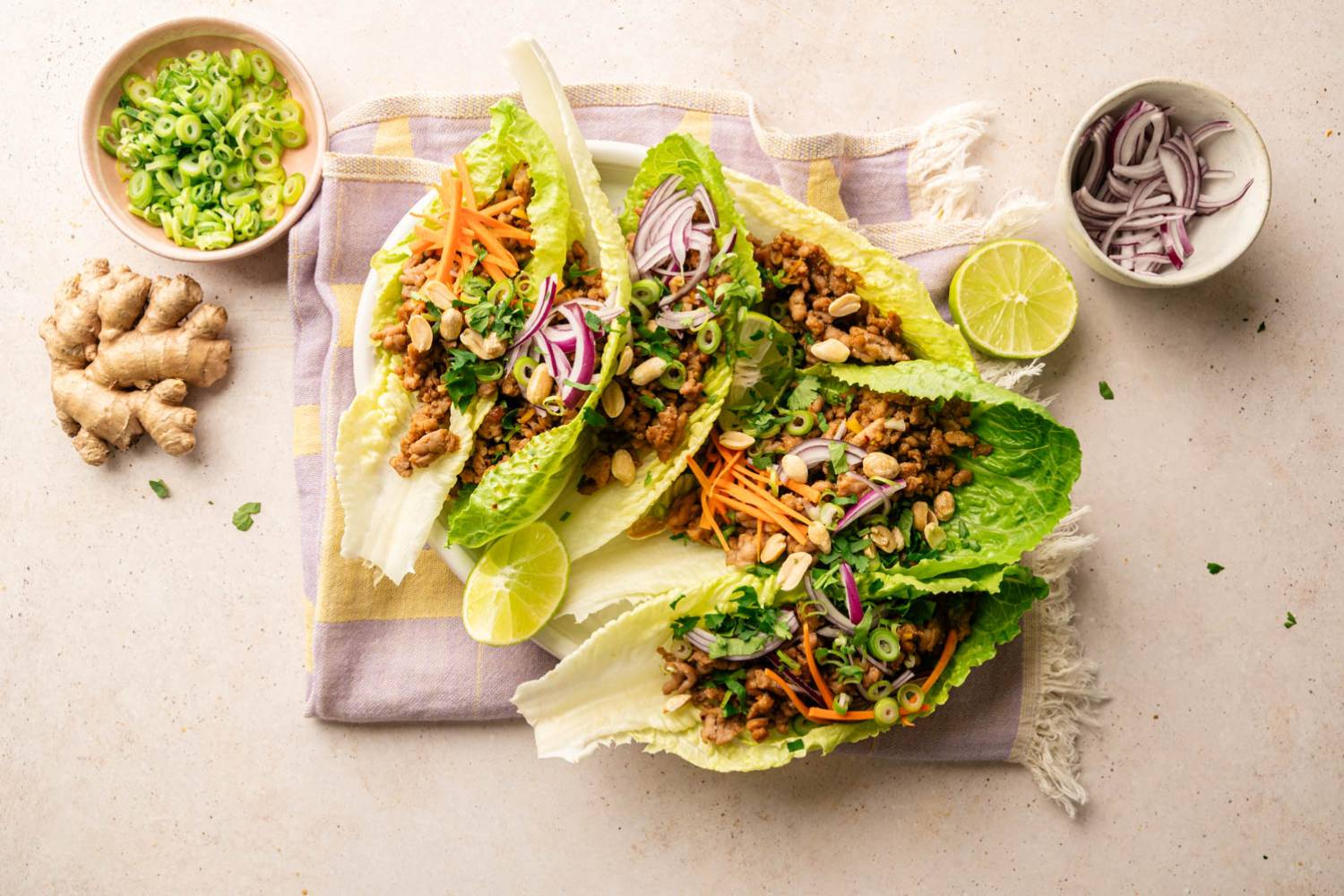 Thai Turkey Lettuce Wraps Thai turkey lettuce wraps served in crisp romaine leaves and topped with shredded carrots, red onion, green onions, cilantro, peanuts, and lime wedges on a white plate.