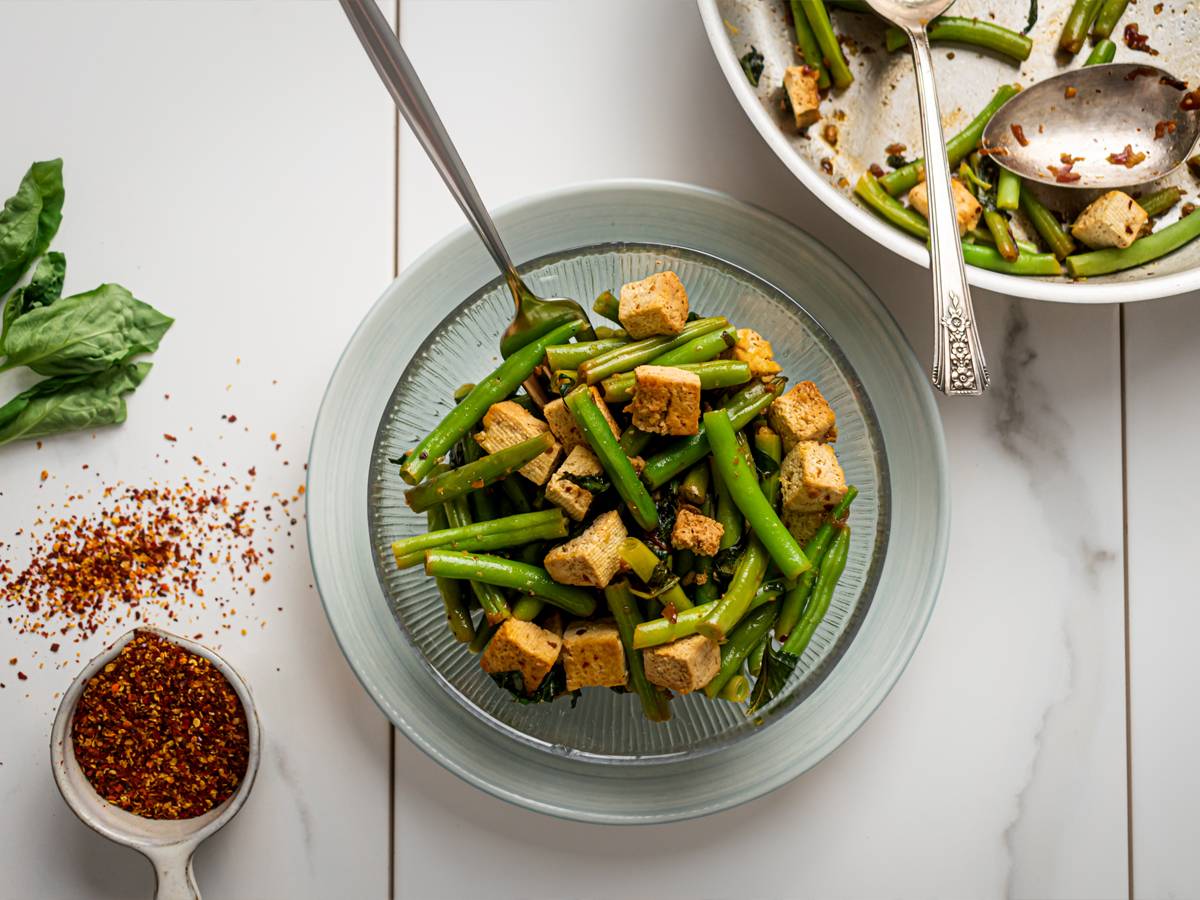 Basil tofu with green beans in a glass bowl with a skillet on the side.