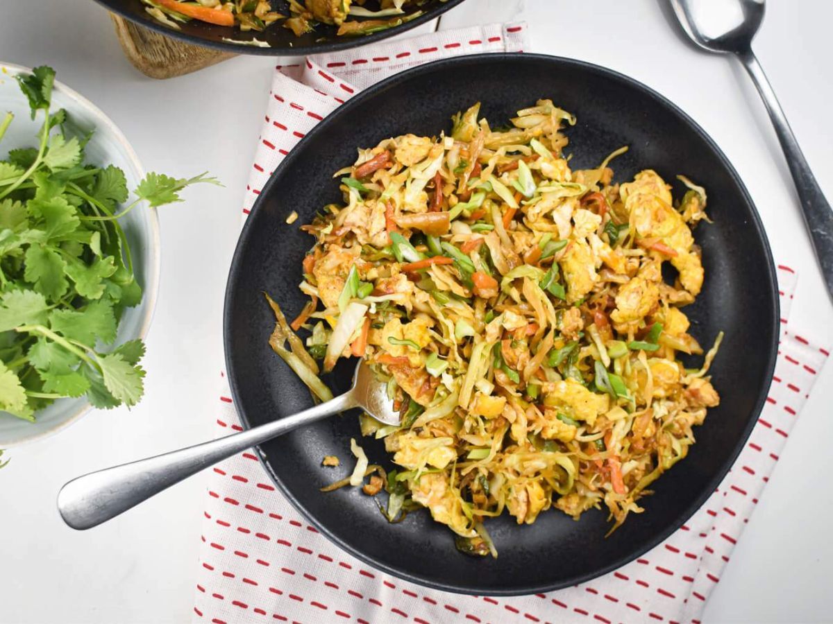 Cabbage fried rice with shredded cabbage, carrots, green onions, eggs, and soy sauce on a black plate.